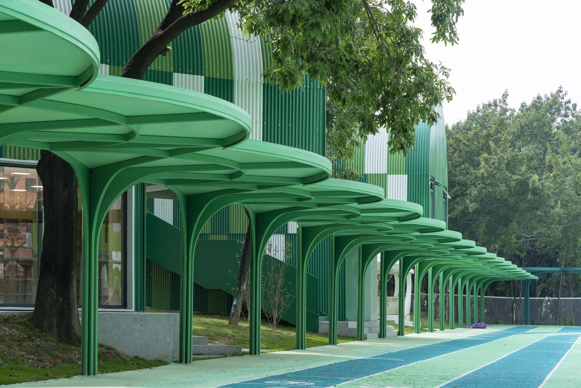 Repeating green arched canopies with ribbed undersides extending along the planted edge of the playground