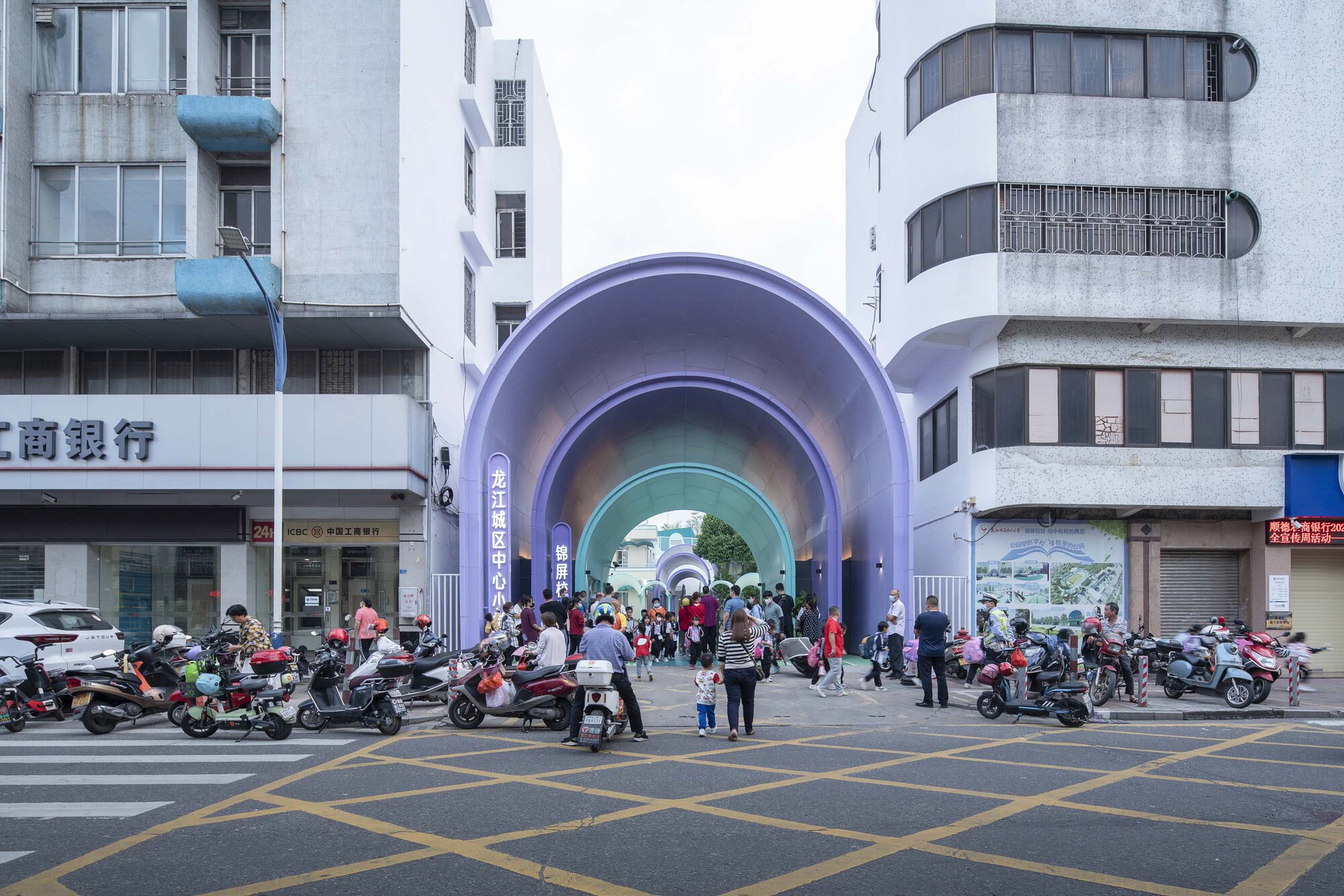 Street view of the layered purple arched entrance portal with pedestrians and parked motorcycles