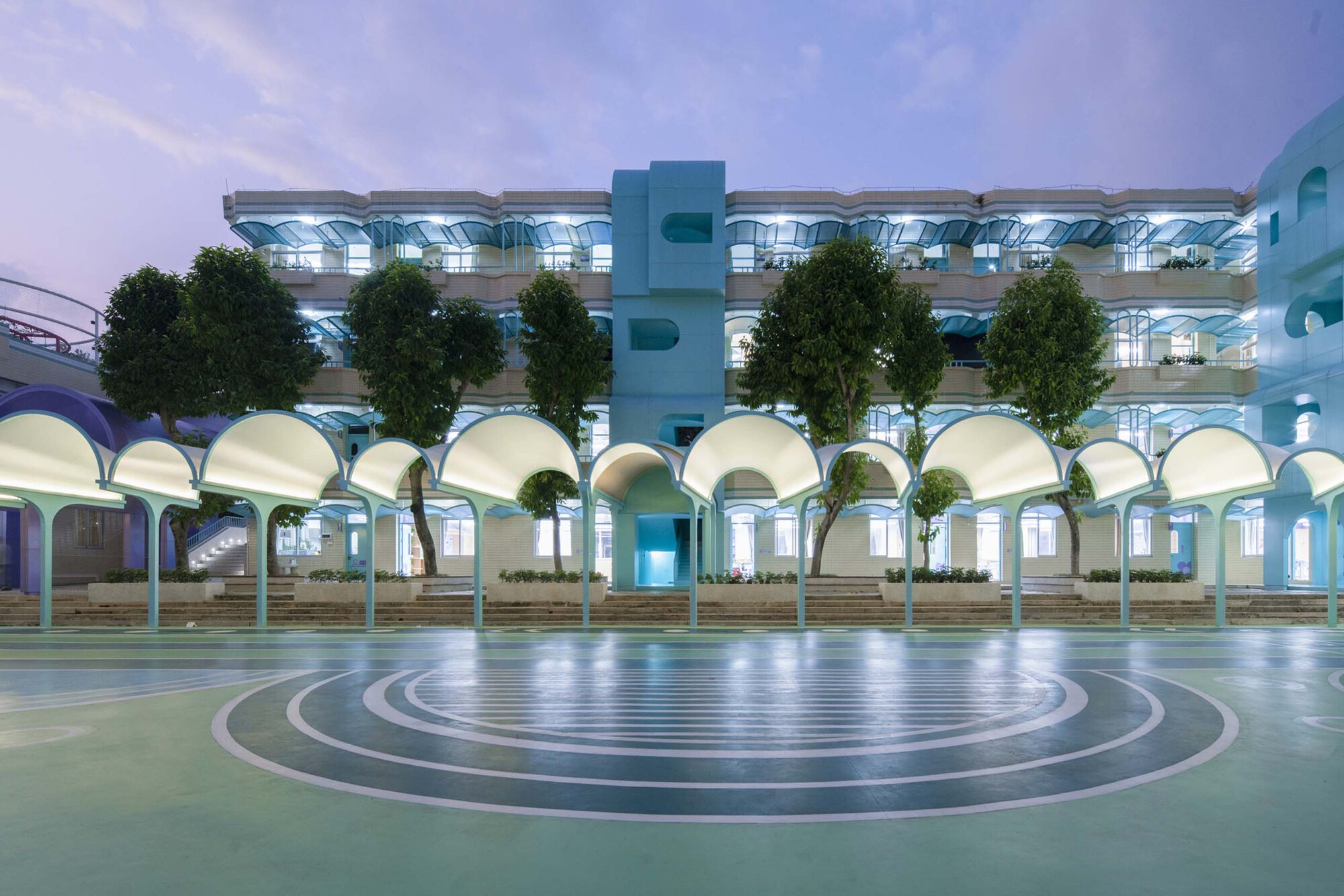 Courtyard with concentric circular paving and a multi-story arcade of vaulted arches under dusk light