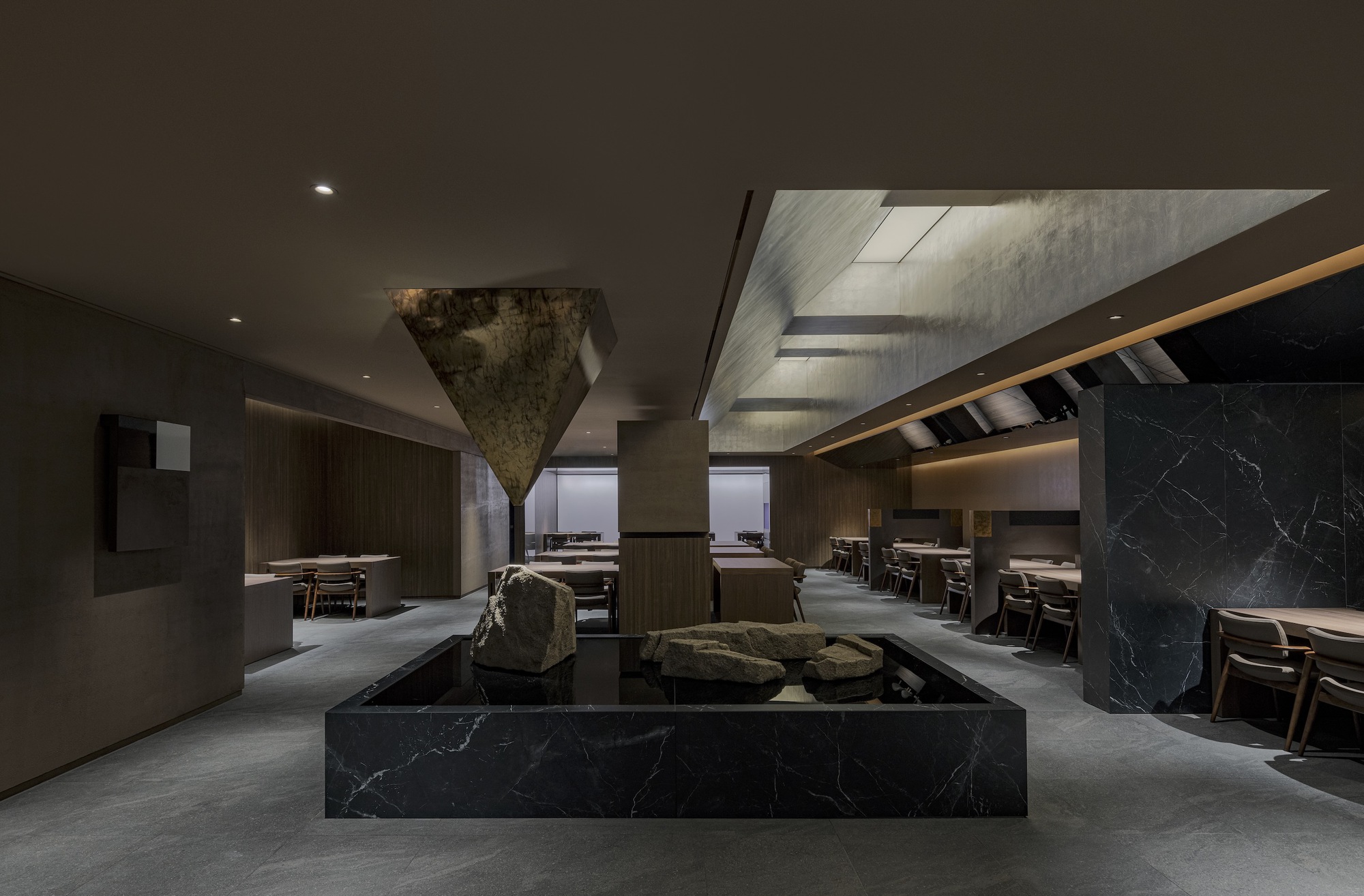 Dining hall interior with inverted pyramid skylight above a black marble plinth holding natural rocks