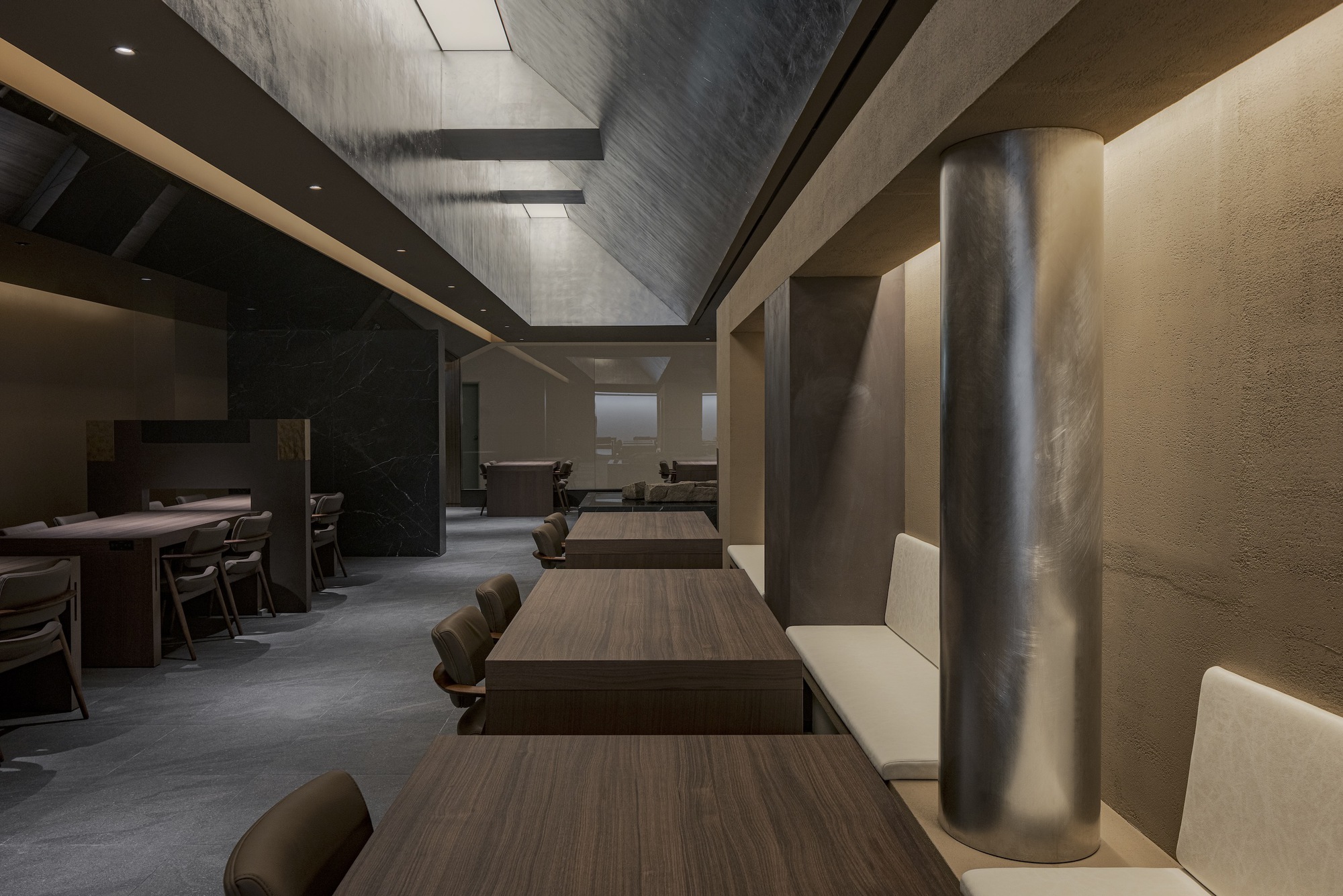 Long view through the dining hall with timber tables and cylindrical column beneath recessed ceiling