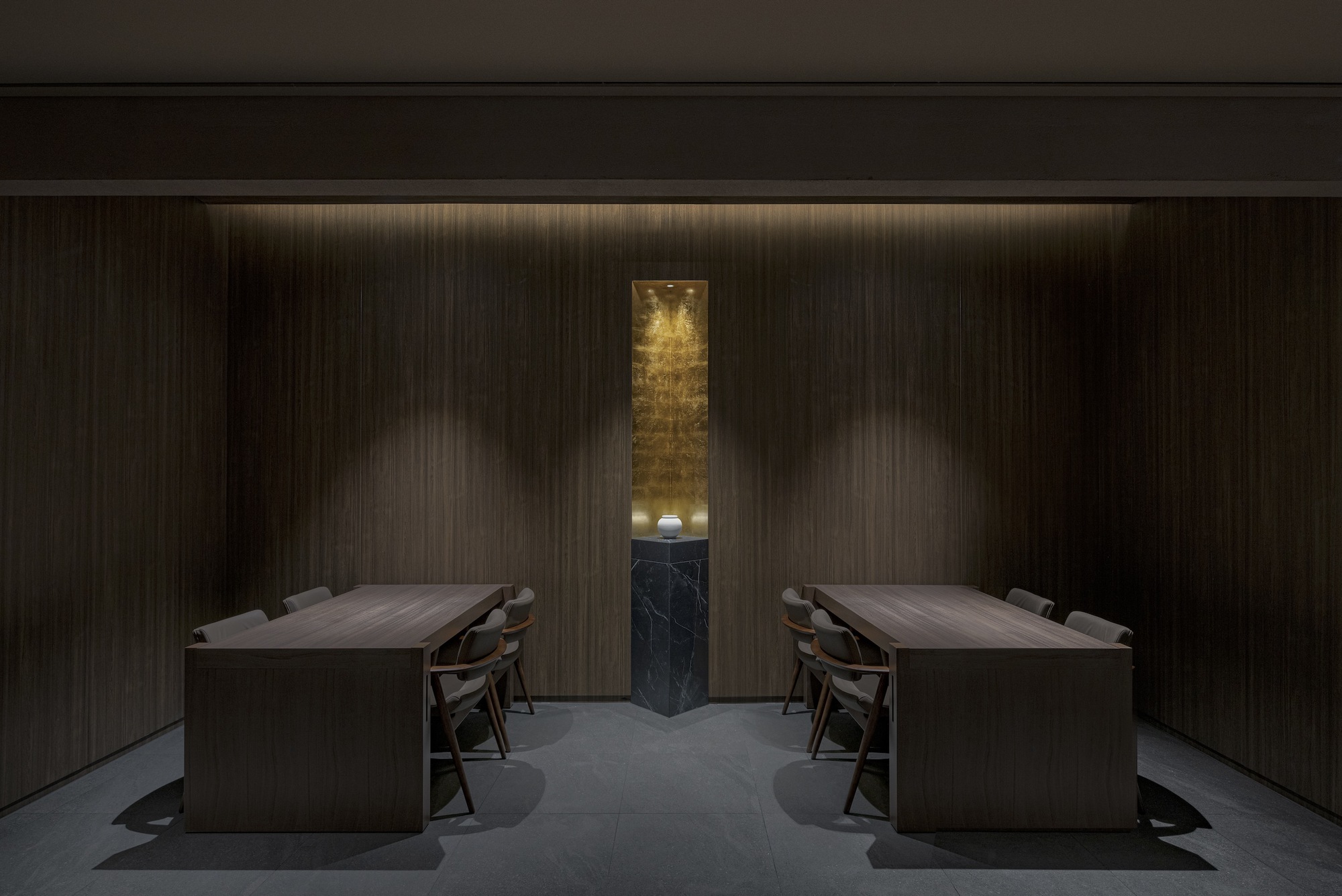 Private dining room with mirrored timber tables flanking a vertical black marble niche with gold leaf
