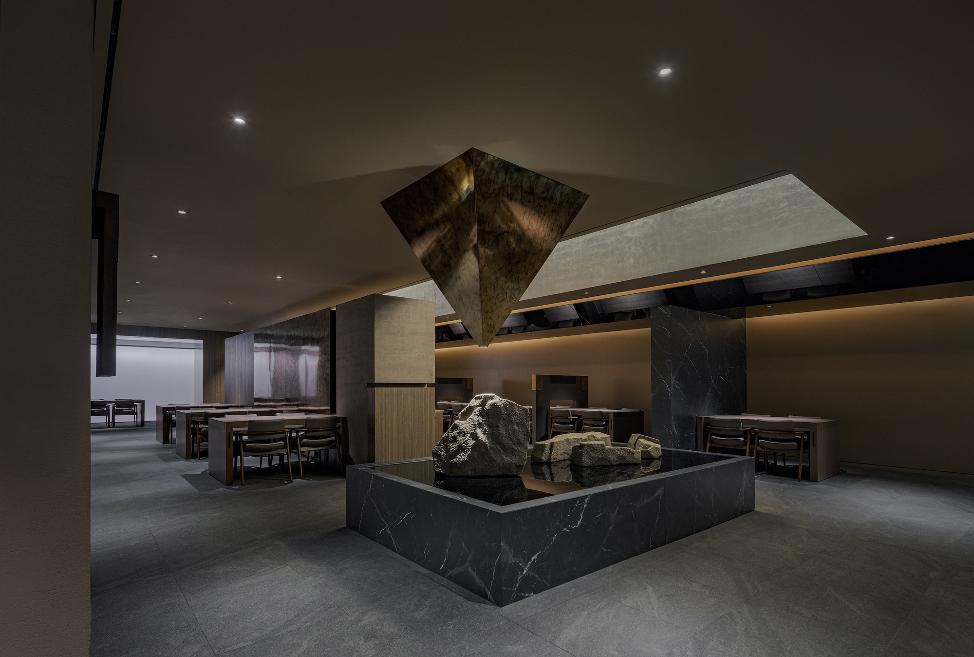 Central black marble plinth with stone sculptures beneath an angular mirrored ceiling element