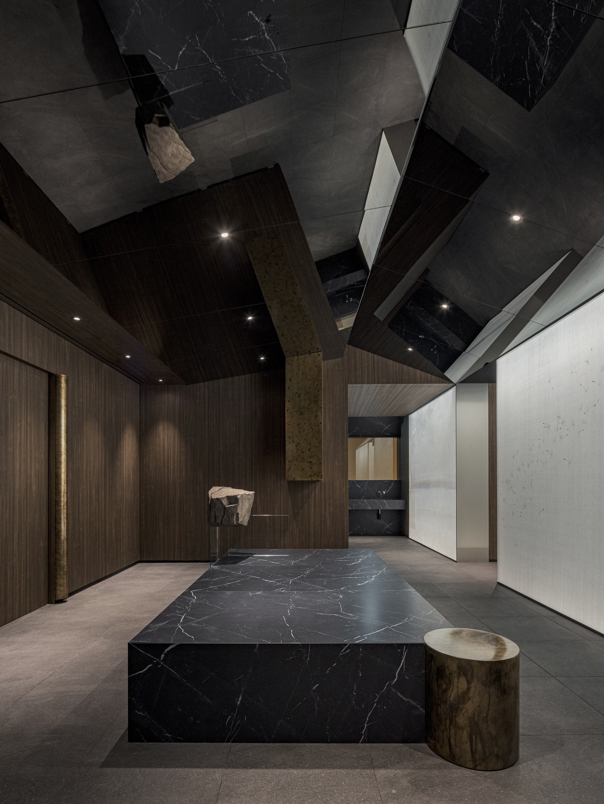 Entry area featuring the marble platform and cylindrical brass stool under geometric ceiling panels