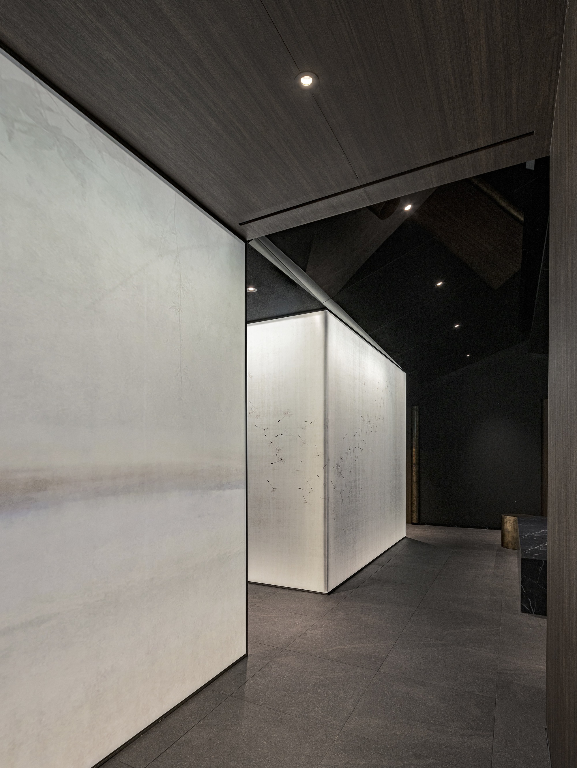 Corridor with pale stone wall panels and timber ceiling leading past a pivoting corner volume