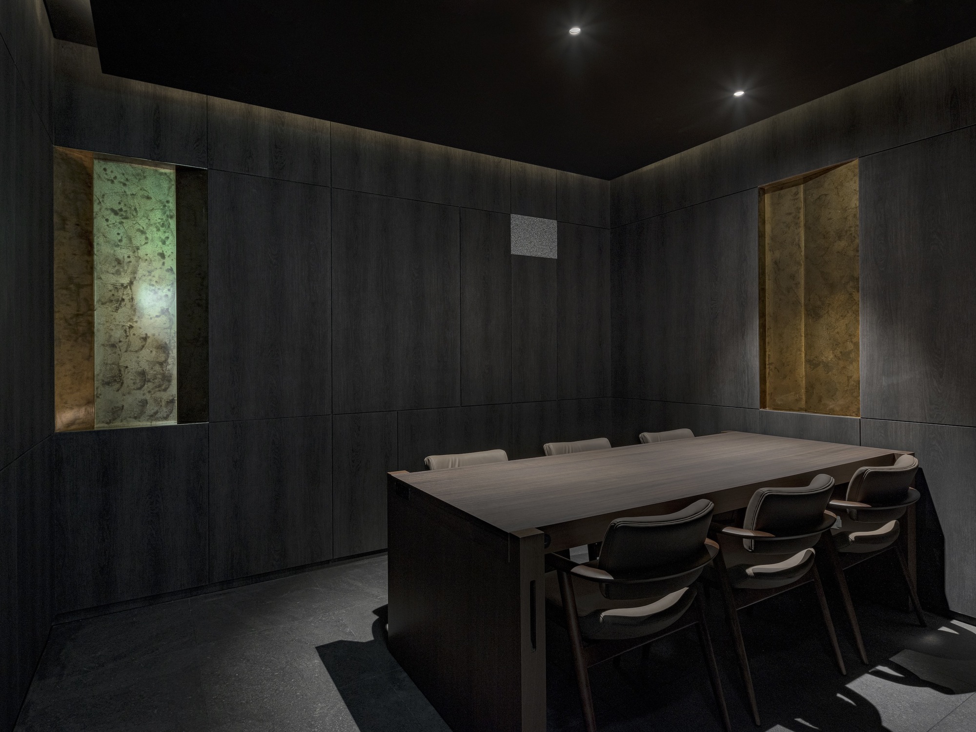 Private dining room with dark timber-paneled walls and backlit stone panels flanking the table