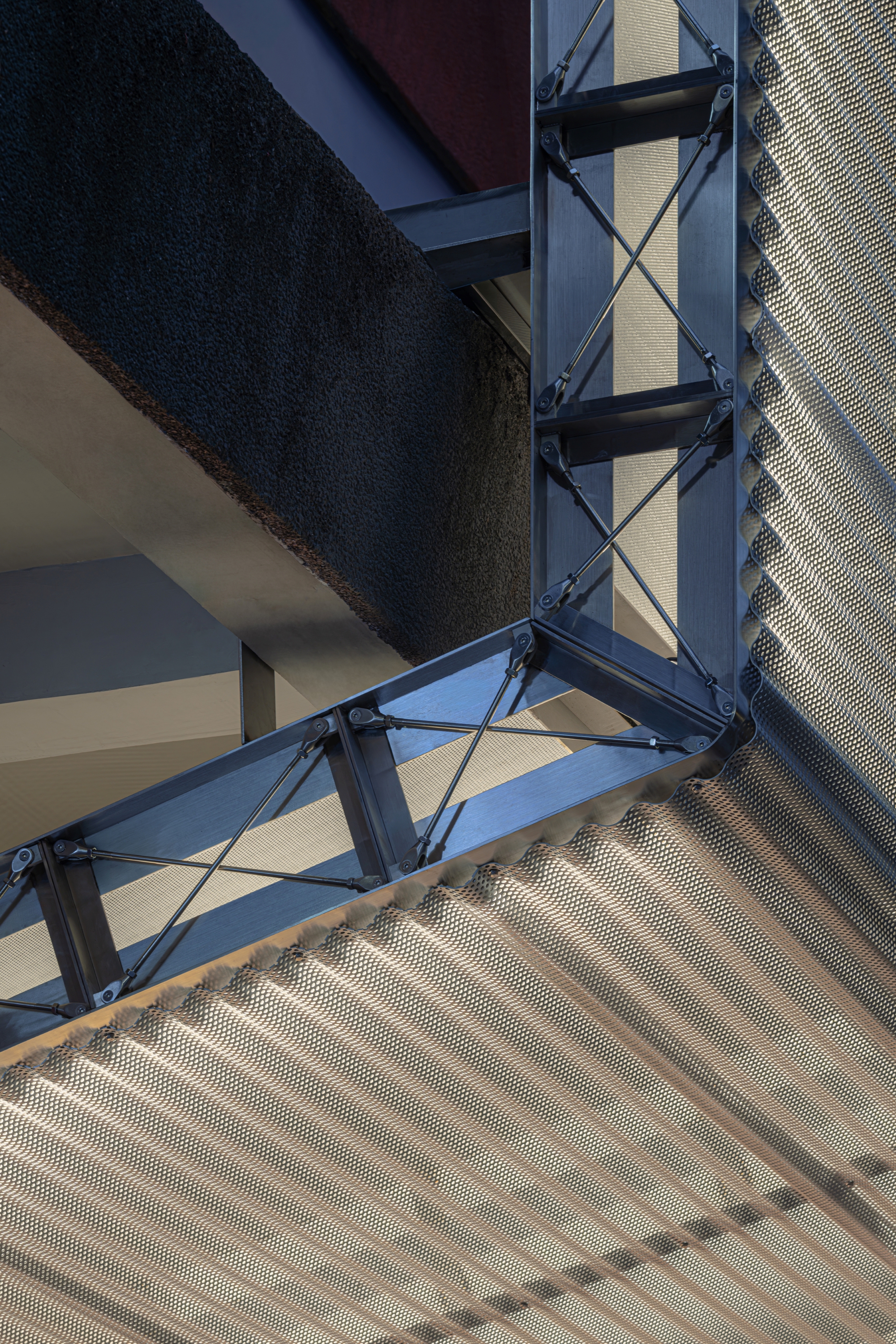 Upward view of steel bracing and corrugated metal ceiling panels in afternoon light