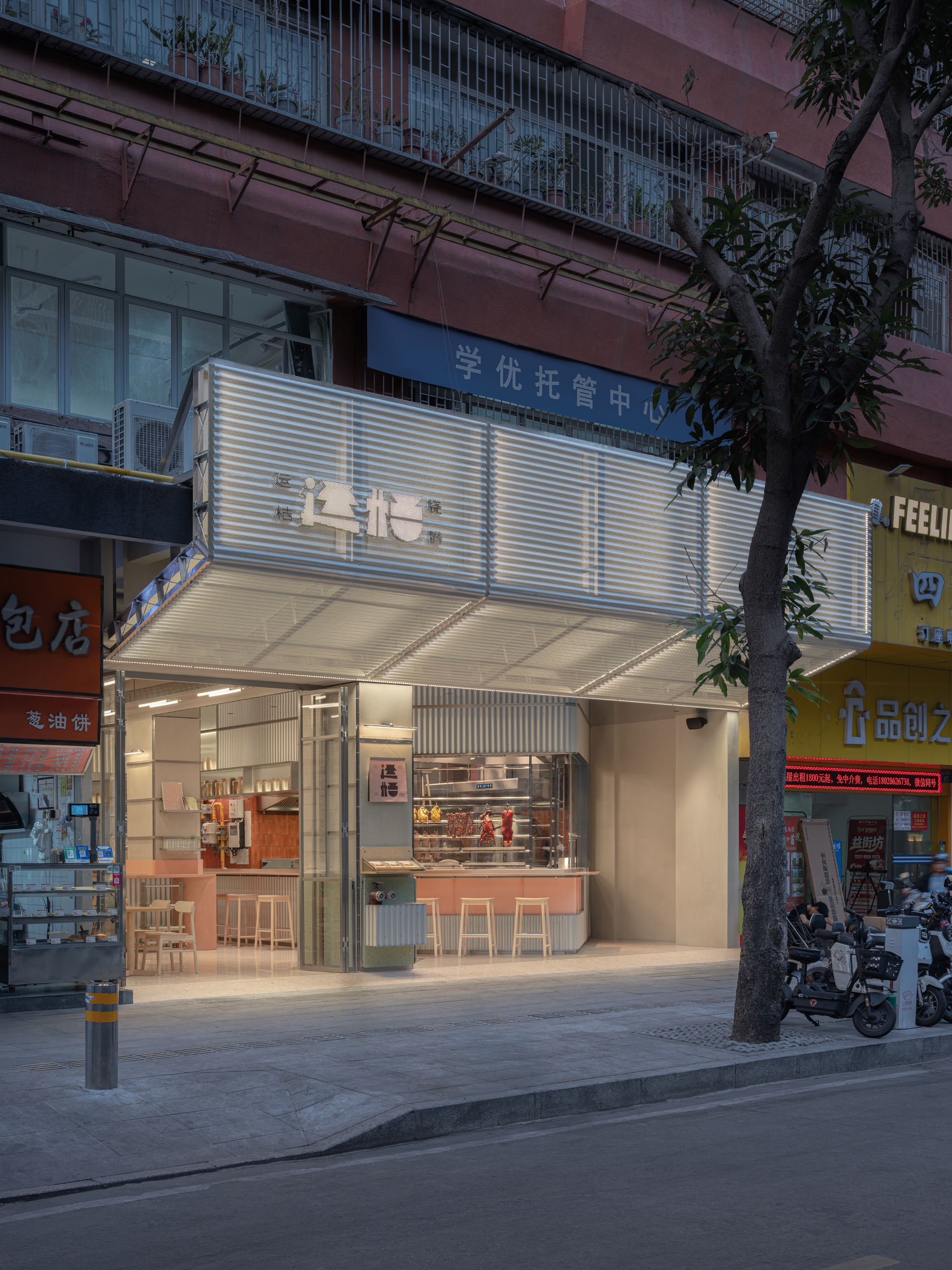 Angled view of the shopfront facade showing corrugated metal panels and glazed opening at twilight