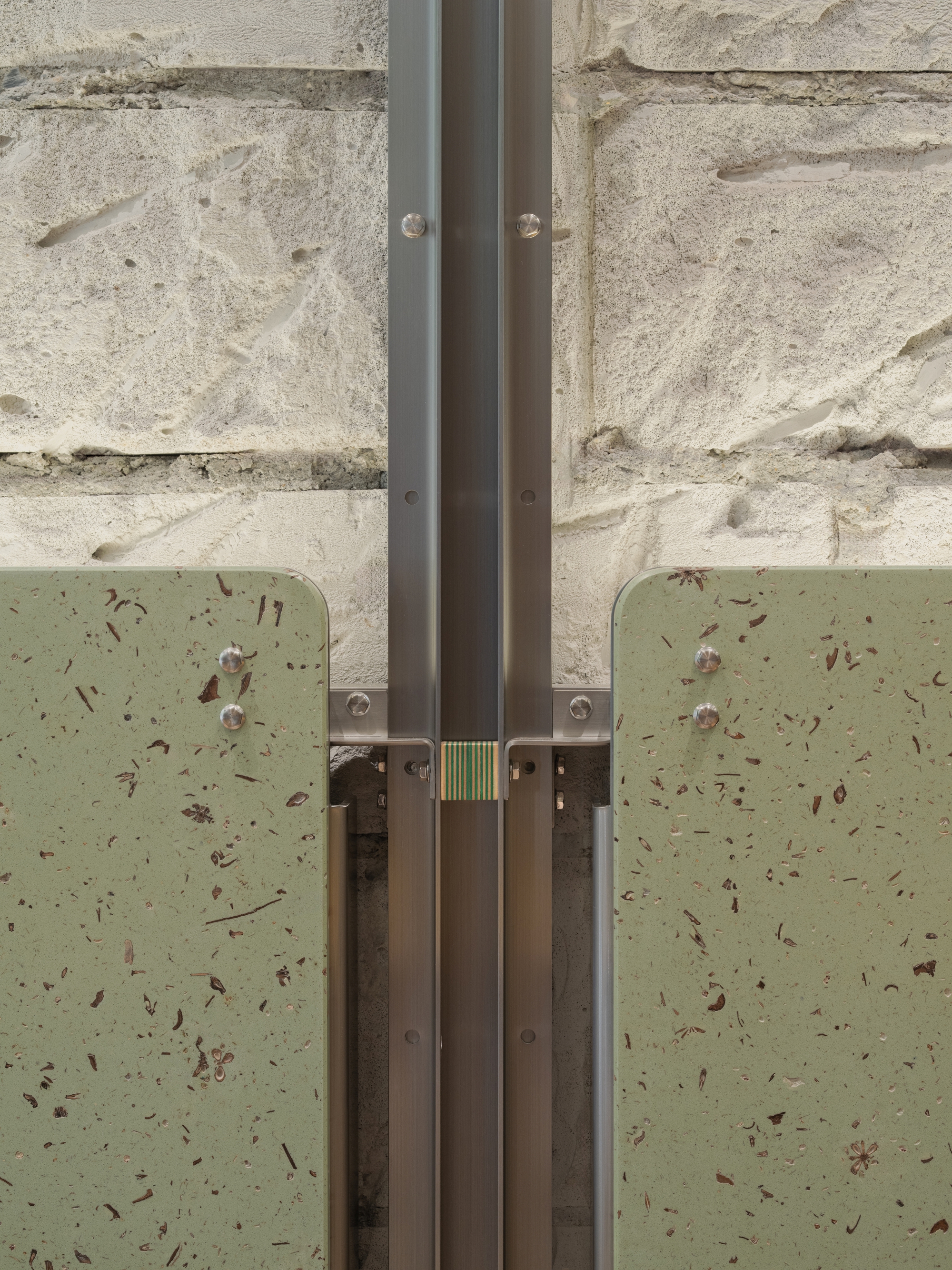 Detail of steel door frame junction with bolted connections against terrazzo panels and concrete block wall