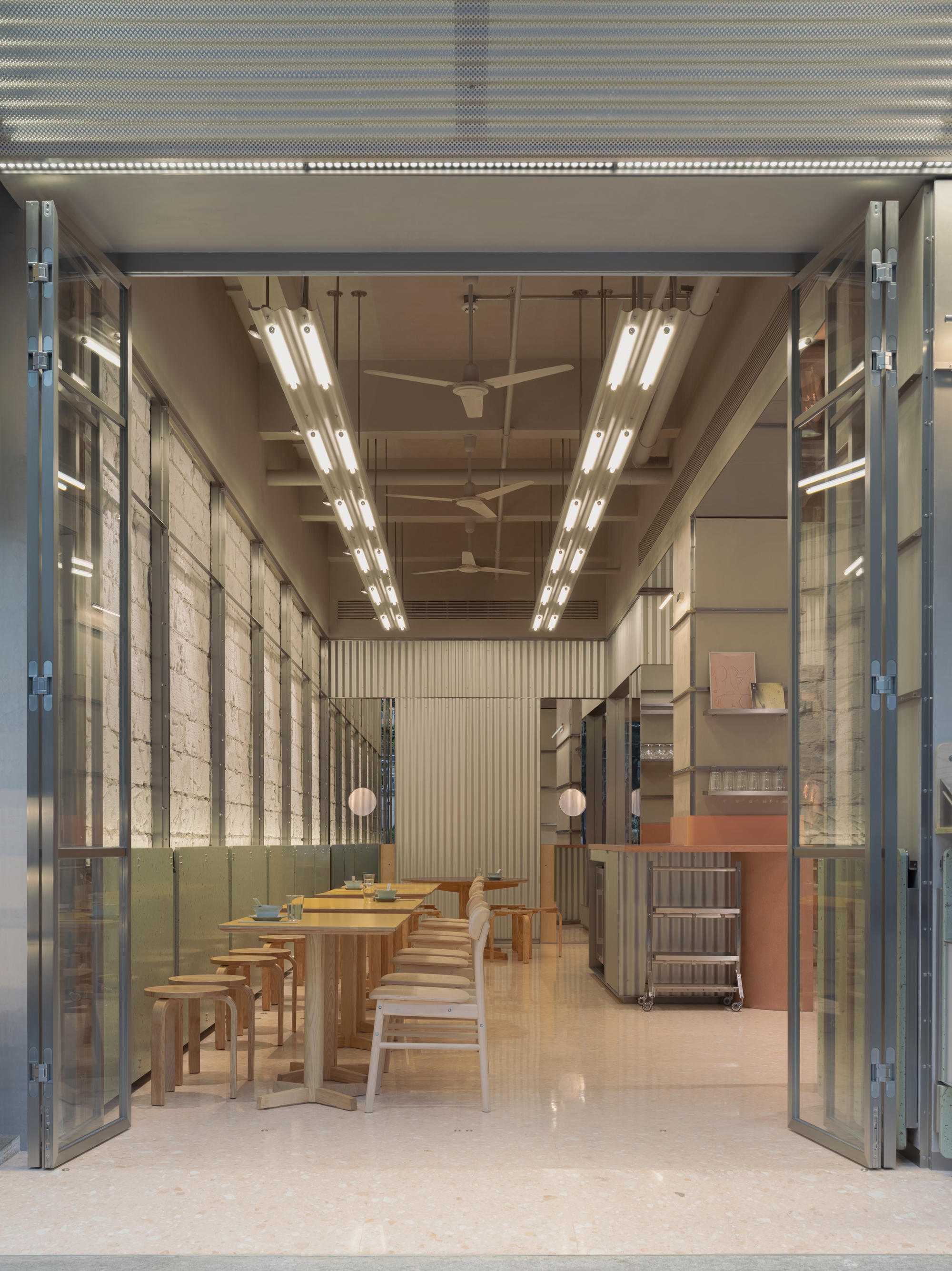 View through steel-framed folding doors into a dining space with exposed timber ceiling and linear lighting