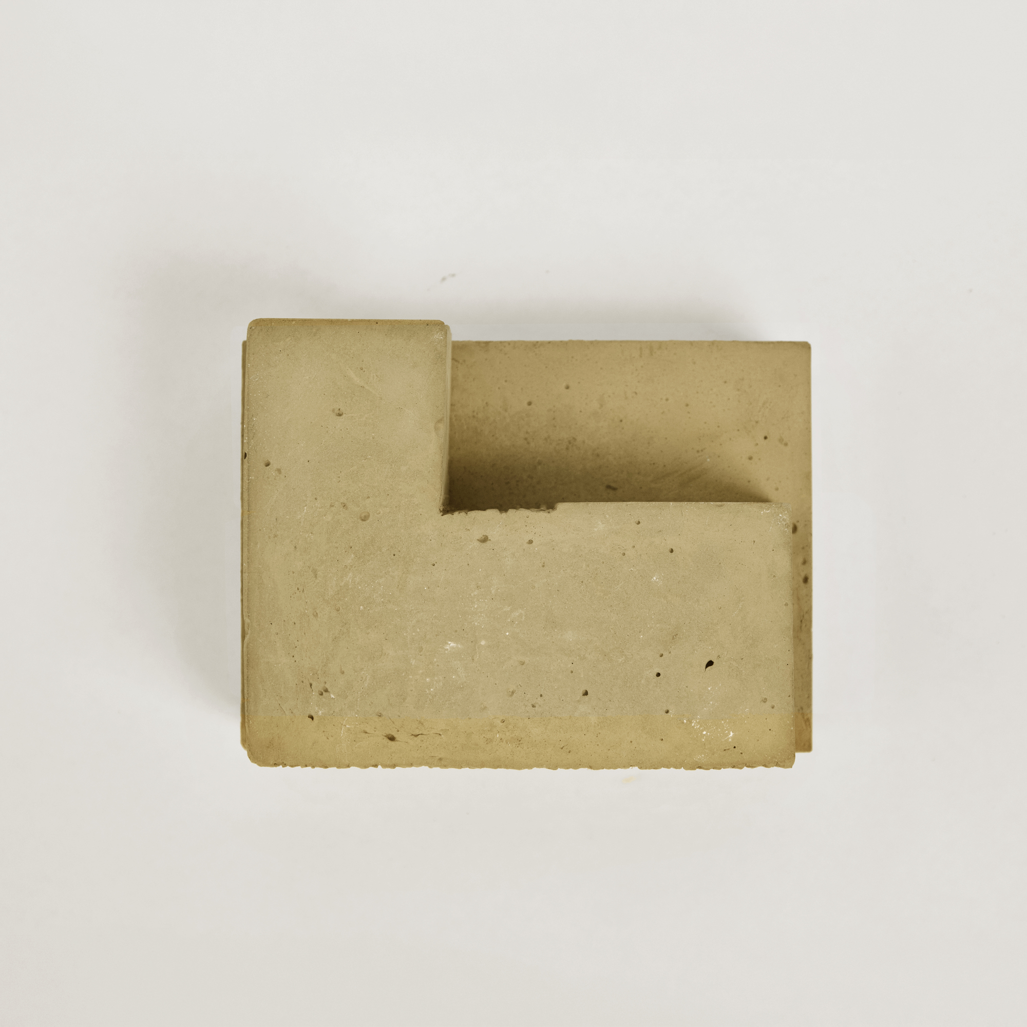 Top-down view of a cast concrete sample with an L-shaped void on a white surface