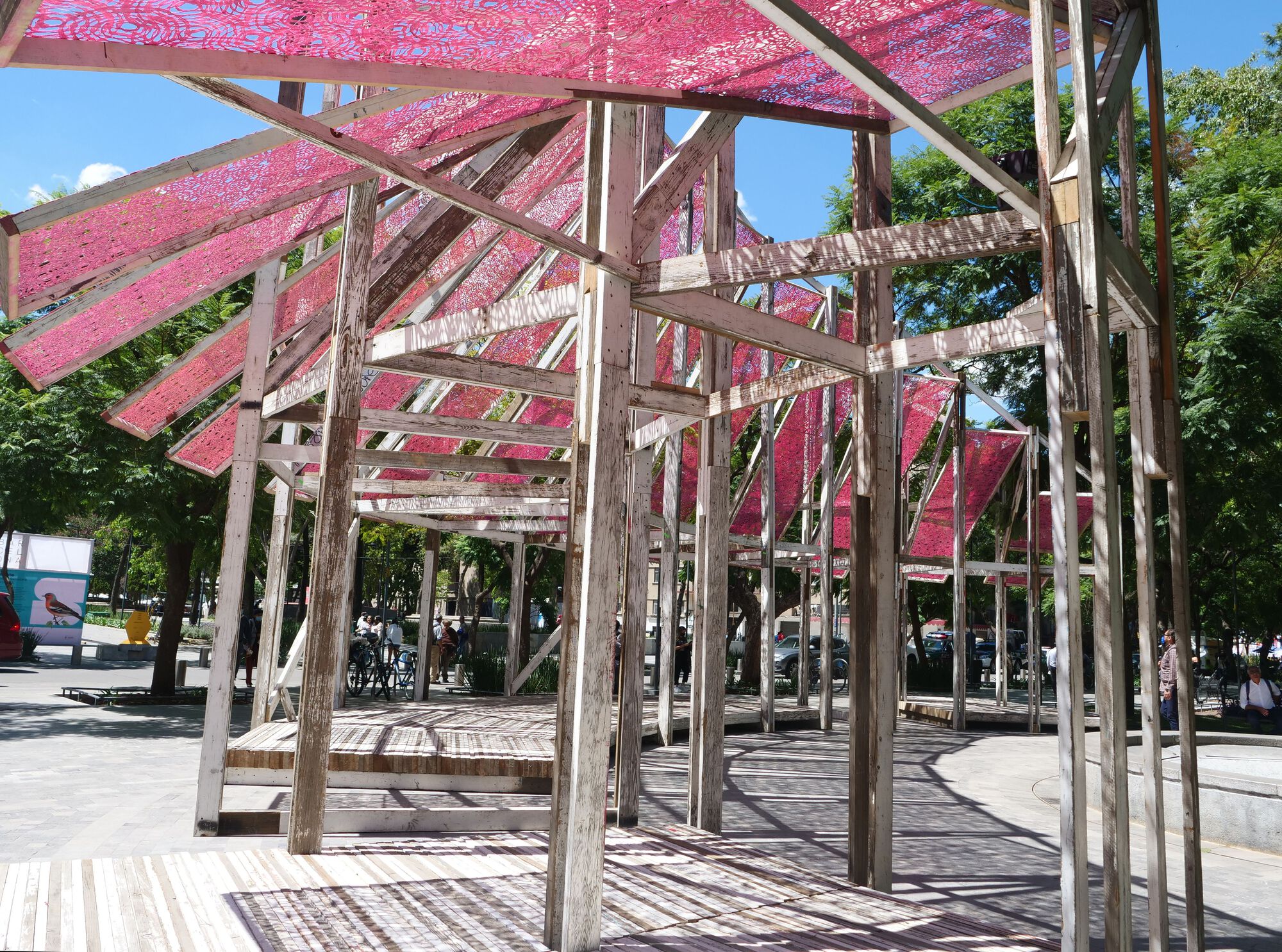 Interior view beneath the angled timber frame structure showing cross bracing and translucent pink canopy overhead