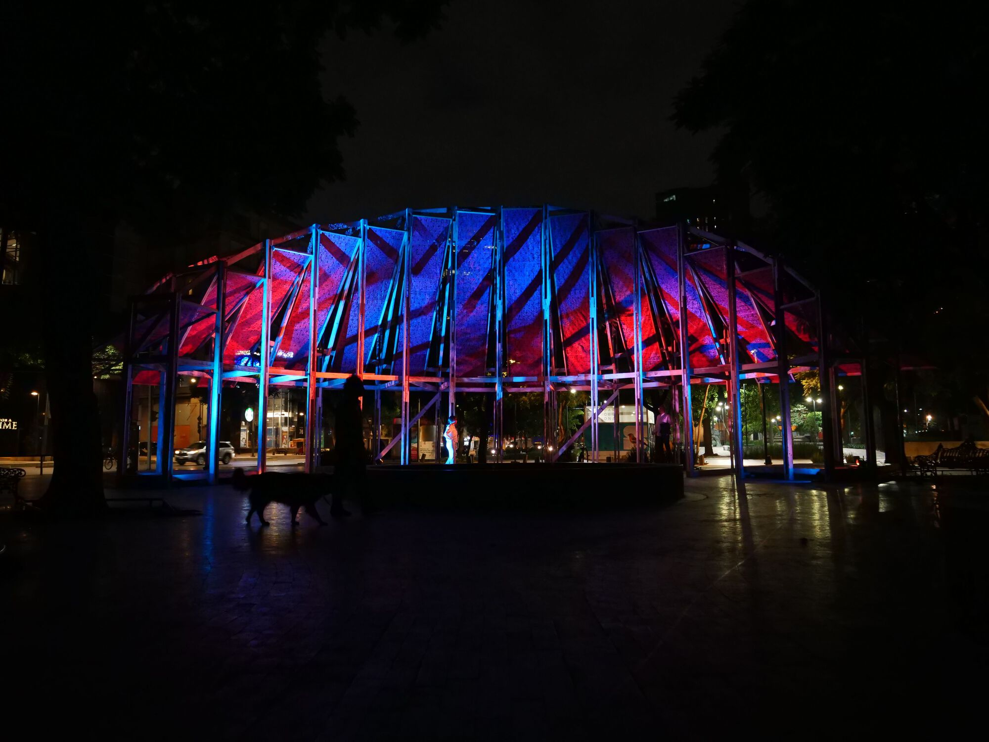 Night view of the illuminated pavilion with blue and red lighting on timber frame and fabric roof