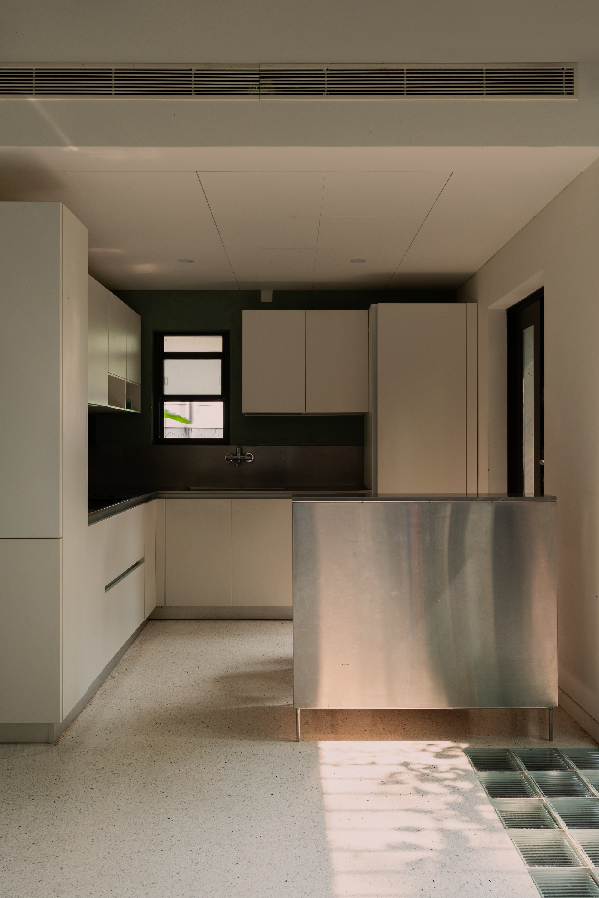 Kitchen with cream cabinetry and steel breakfast counter above terrazzo floor with green tile inset