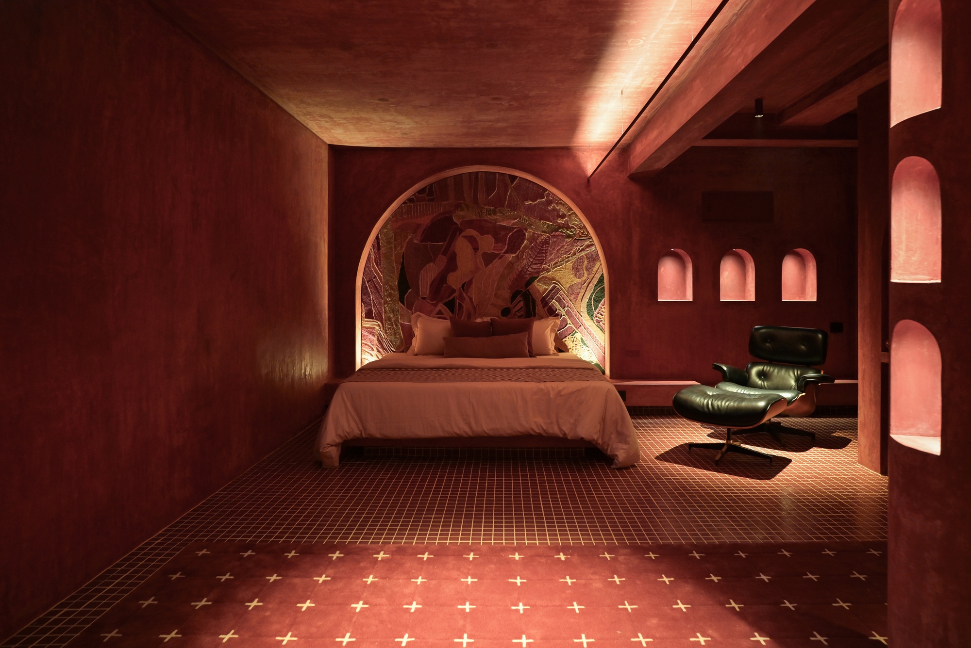 Bedroom enveloped in terracotta plaster with arched headboard niche and tiled floor with brass inlay