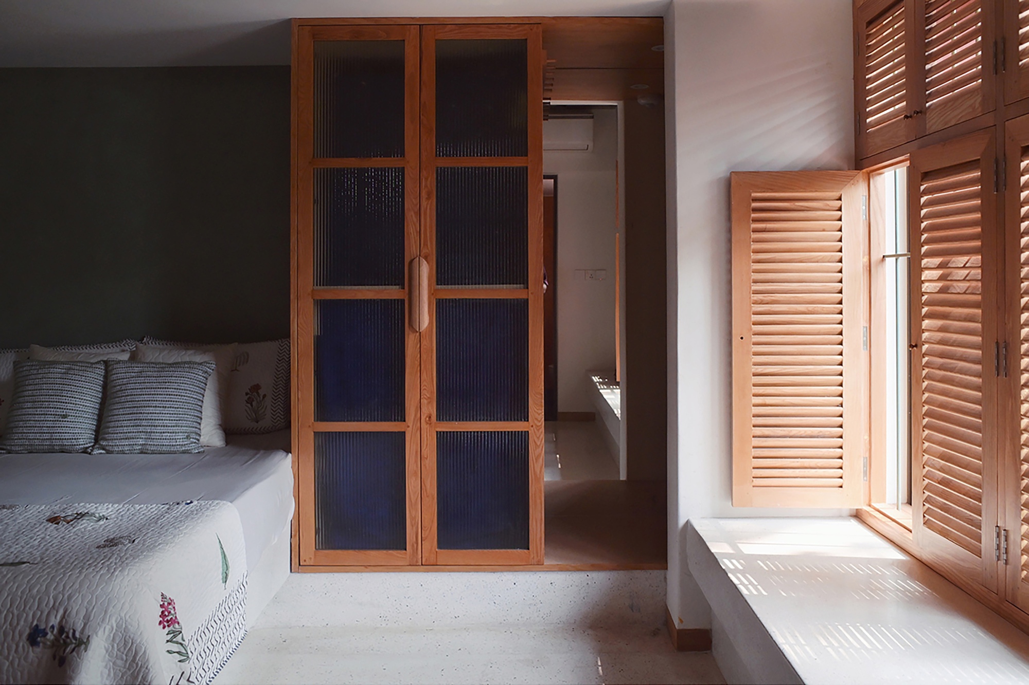 Bedroom with timber-framed glass doors and louvered shutters filtering daylight onto pale concrete floor