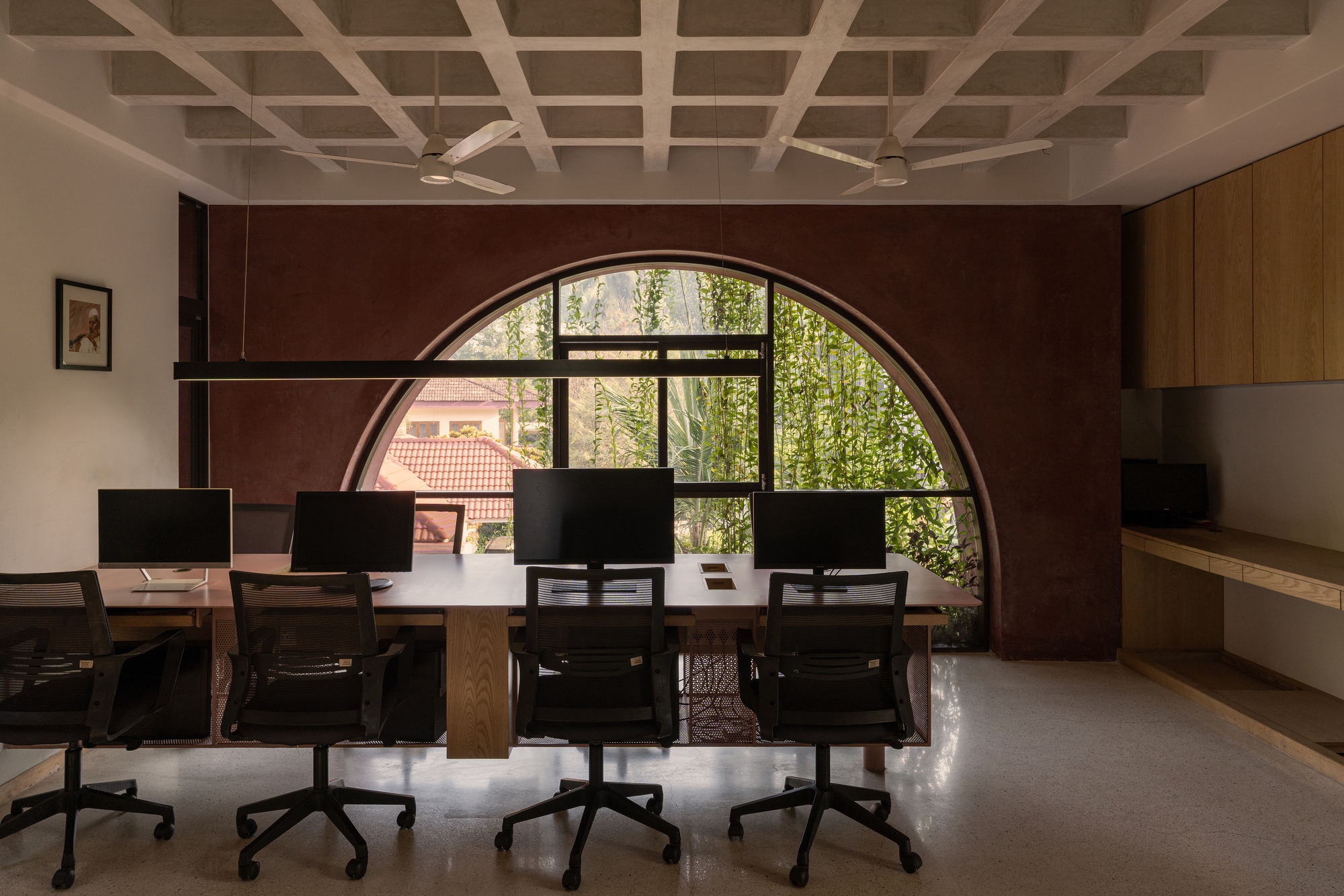 Workspace with coffered ceiling and arched window framed by a maroon wall overlooking greenery