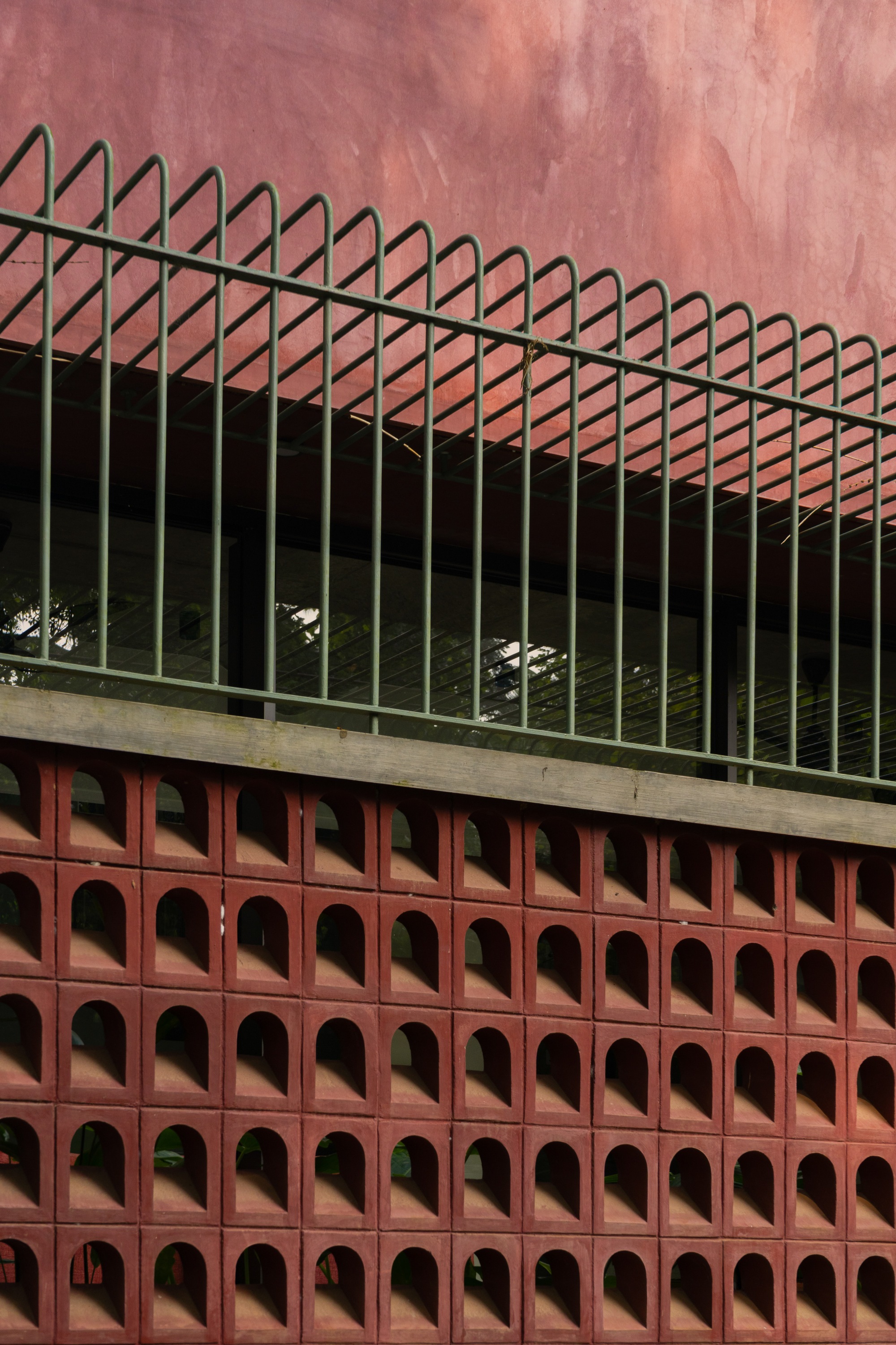 Close-up of the terracotta perforated screen with triangular metal railing above the concrete ledge