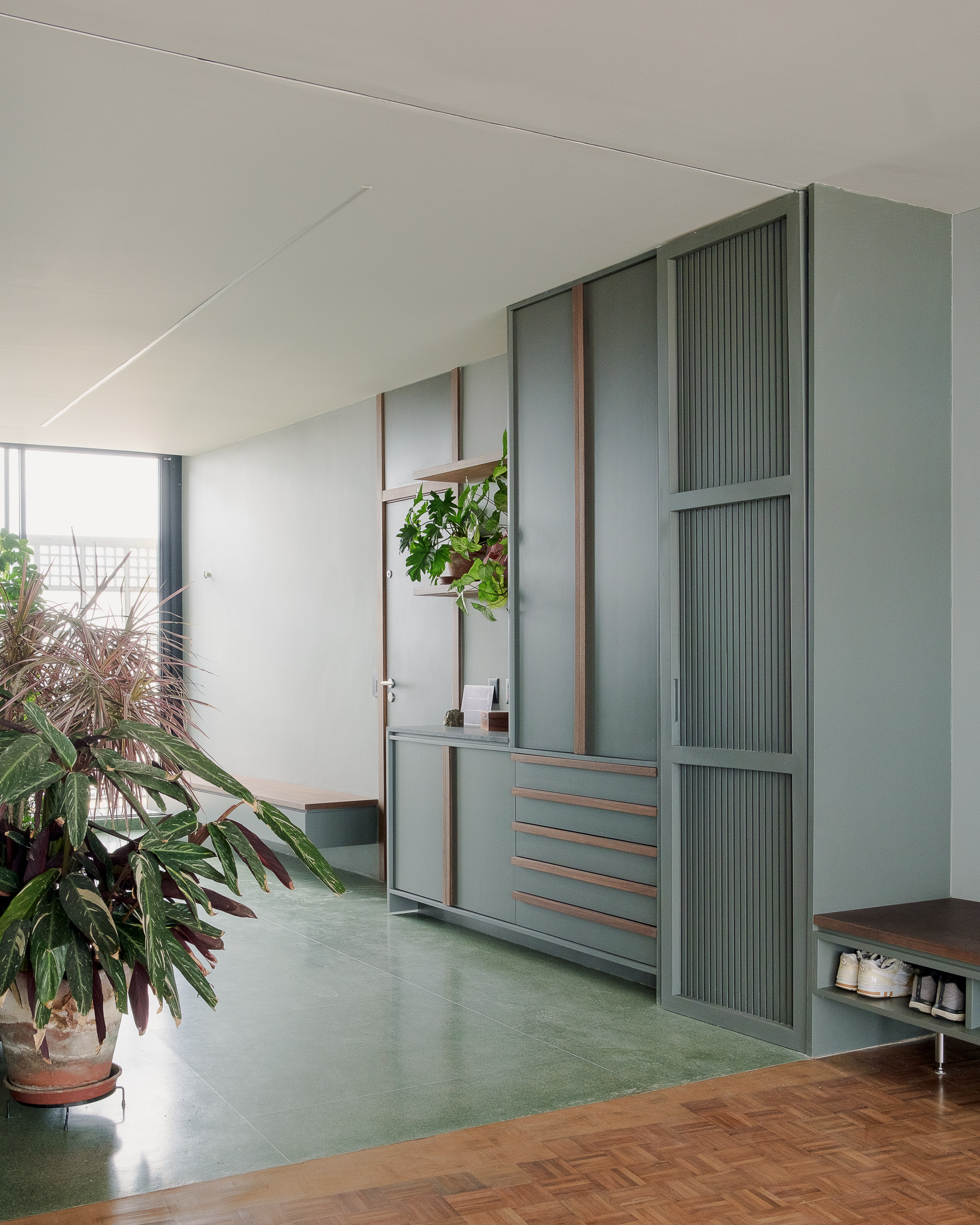 Built-in storage unit with fluted green panels and timber frames beside parquet flooring and potted plants
