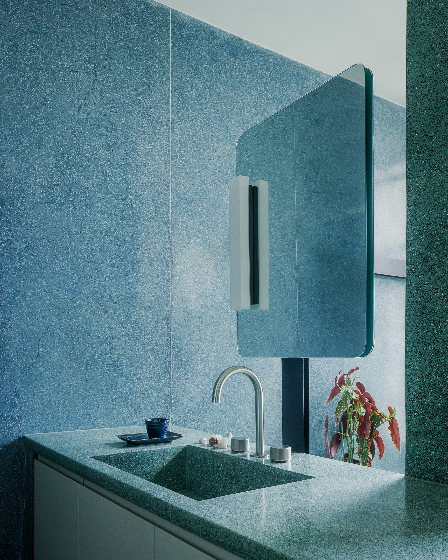 Bathroom vanity with integrated terrazzo sink and rounded mirror against blue mosaic tile walls