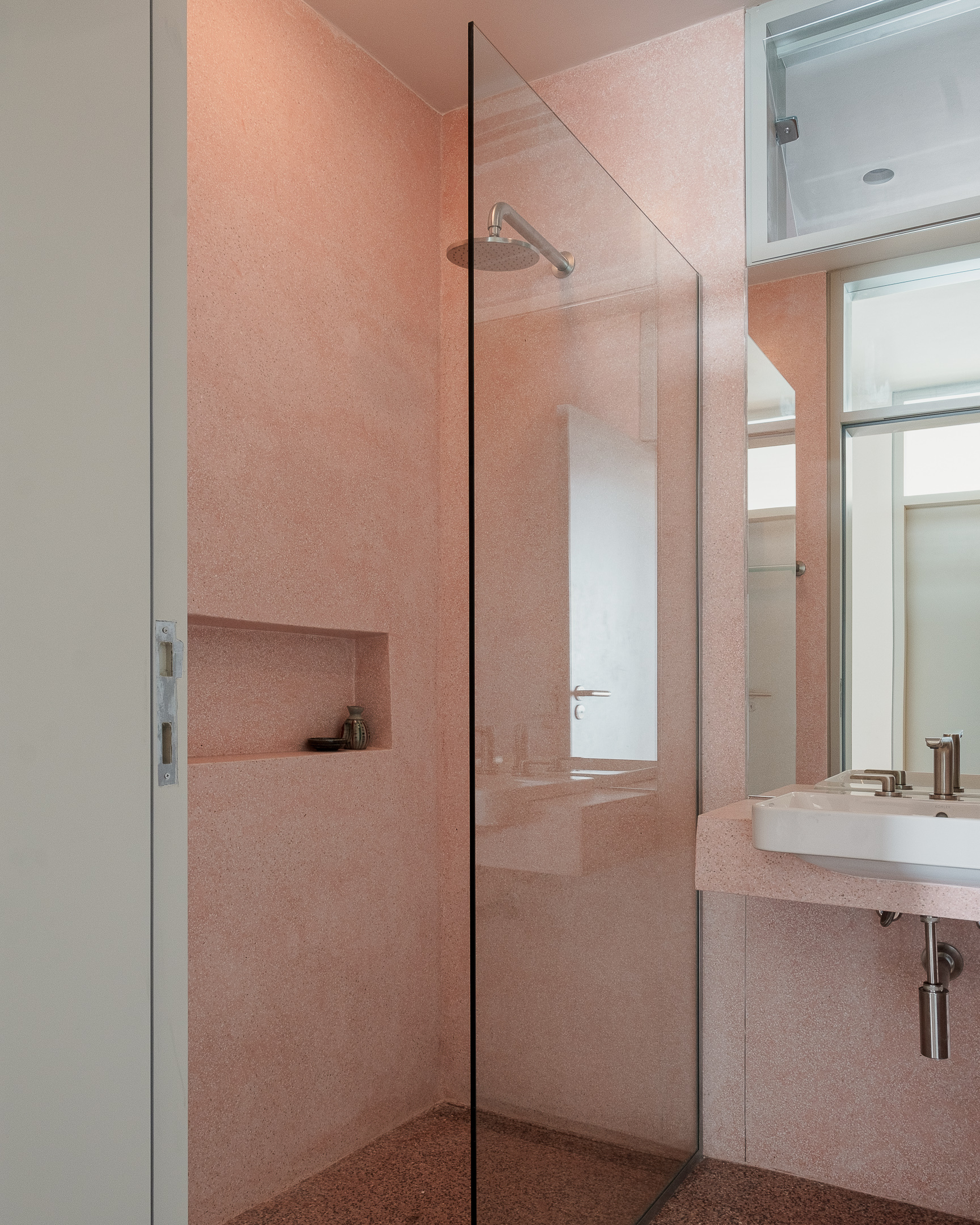 Pink terrazzo bathroom with glass shower partition and recessed wall niche under soft ceiling light