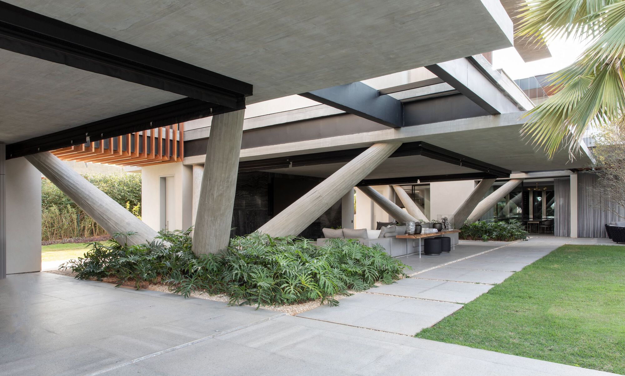Underside of concrete slab supported by diagonal columns sheltering a planted garden and lawn