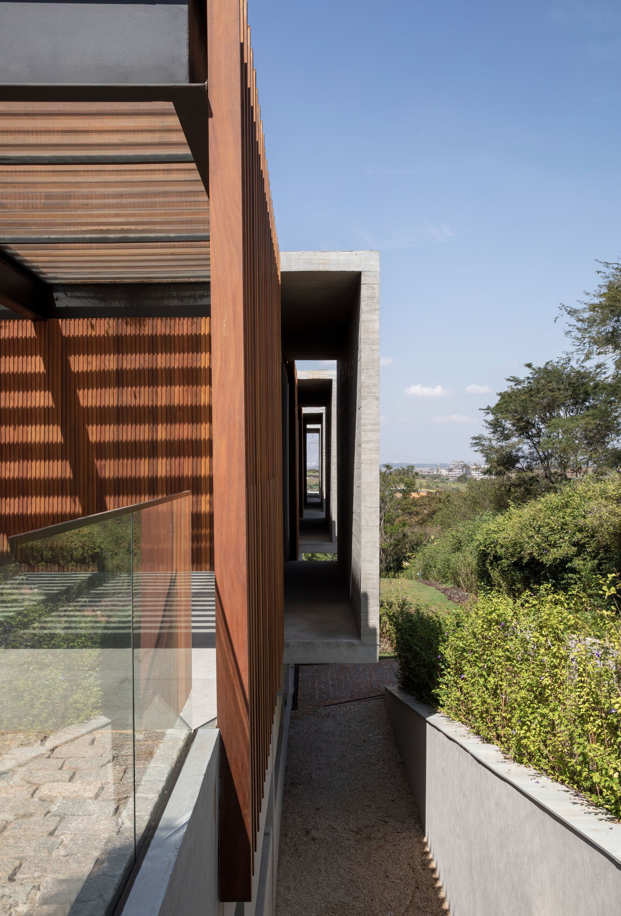 Narrow concrete walkway alongside timber and glass facade with hillside vegetation beyond