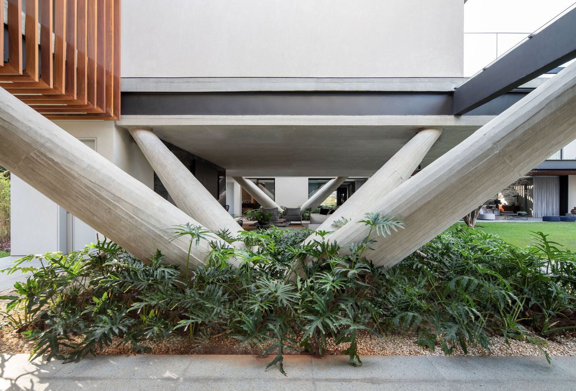 Crisscrossing concrete columns supporting an elevated volume above a planted bed with grasses