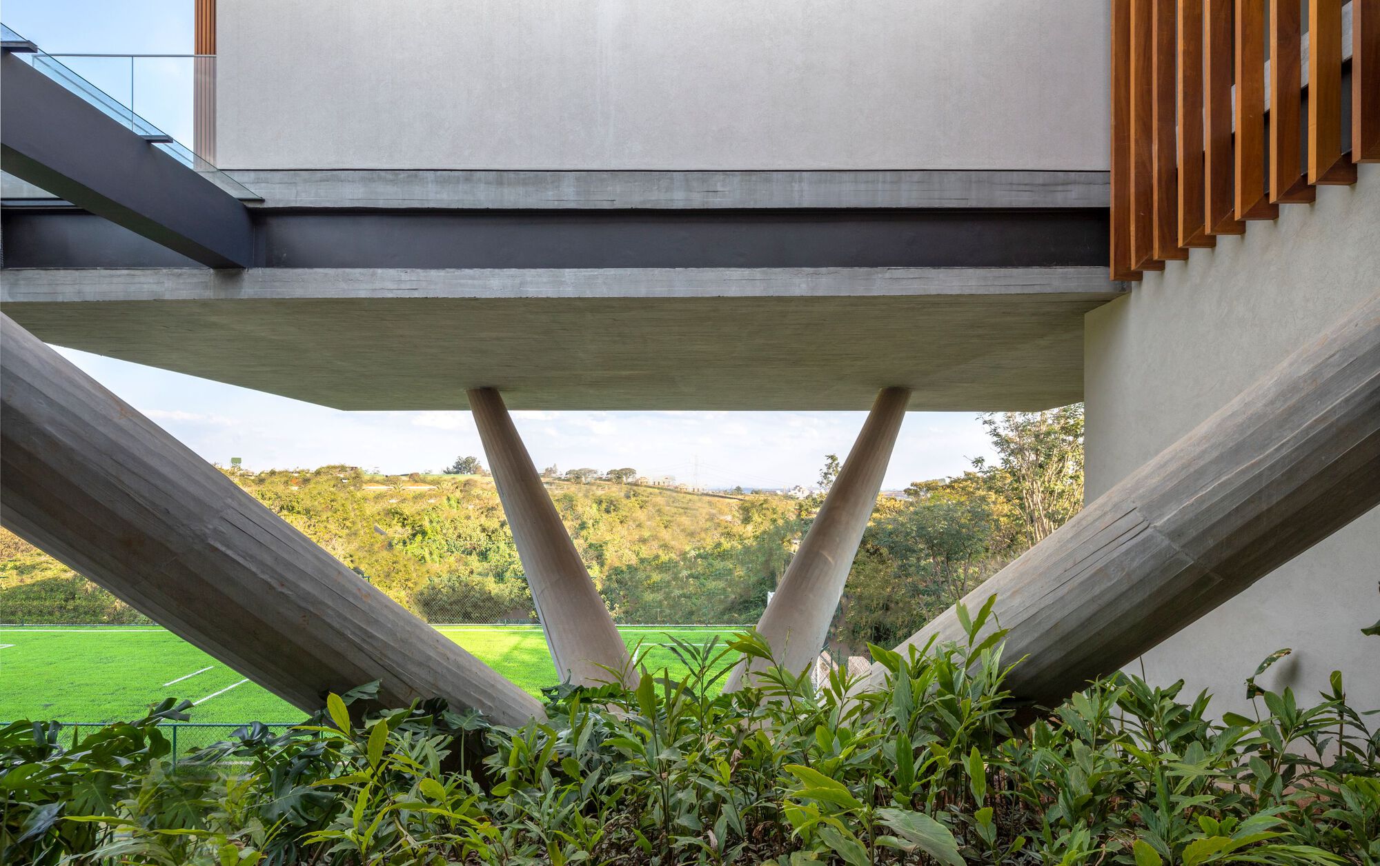 View beneath the cantilevered volume supported by angled concrete columns above a planted bed and lawn