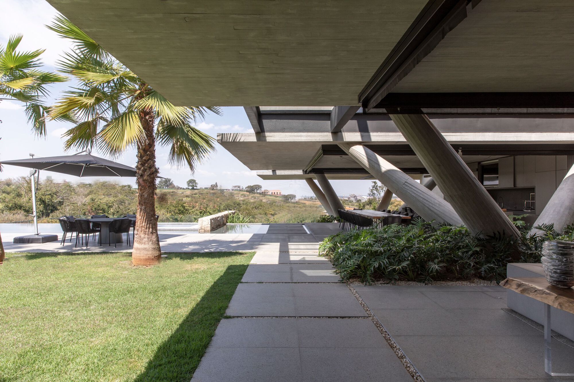 Large concrete pavers crossing the lawn beneath angled structural supports and palm trees