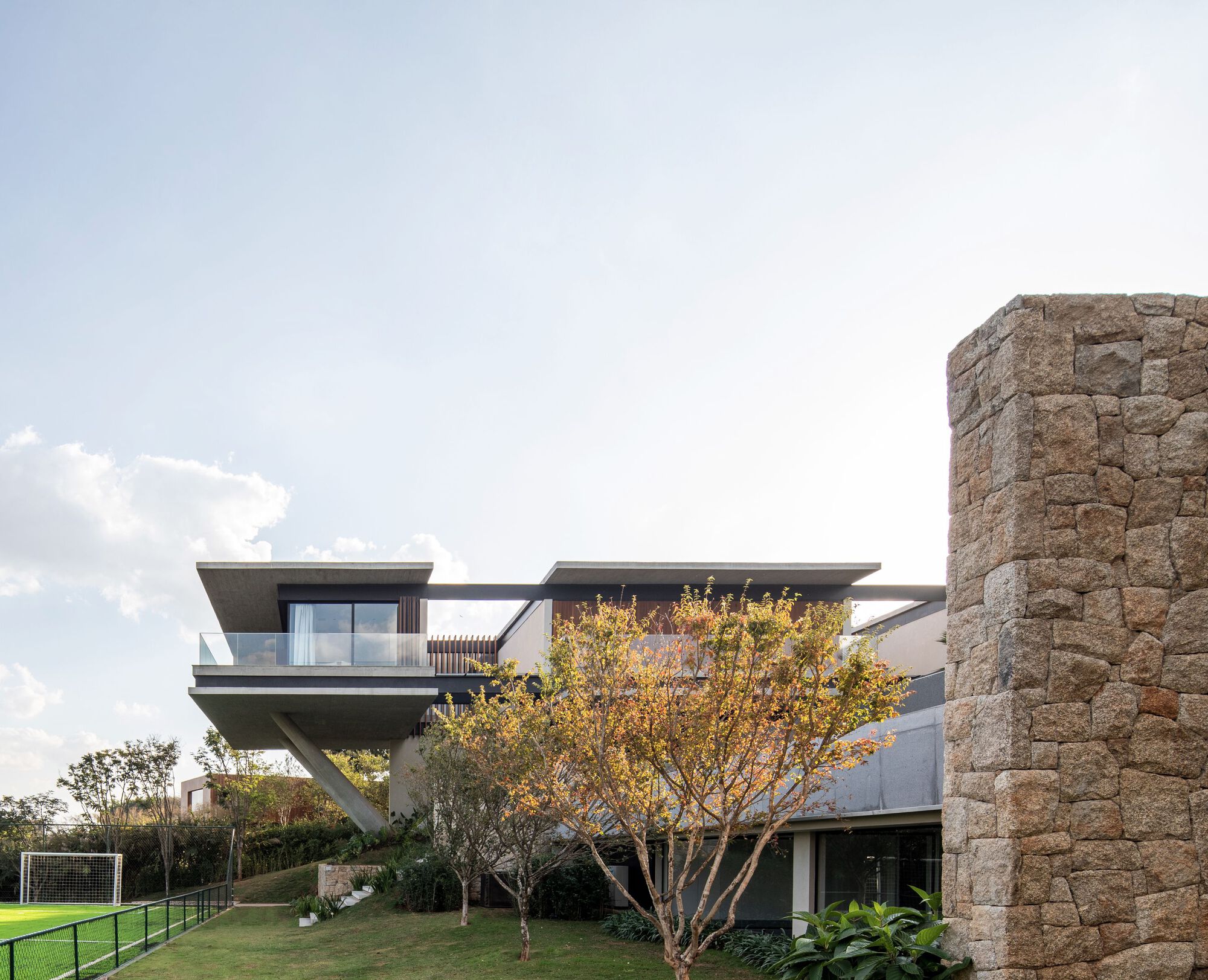 Side elevation showing cantilevered upper levels and rough stone tower beside an autumn tree