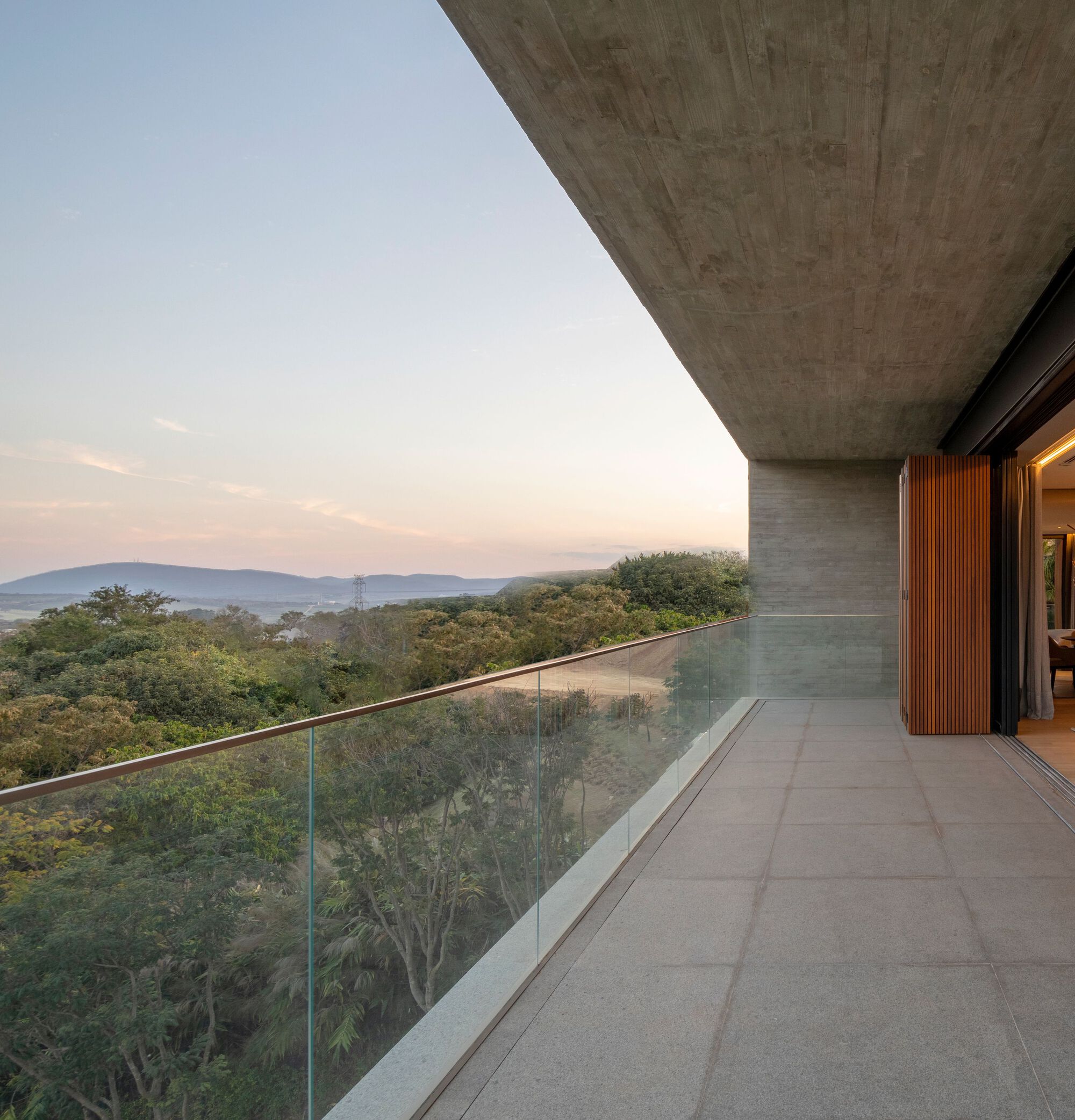 Concrete terrace with glass balustrade overlooking a forested valley at dusk
