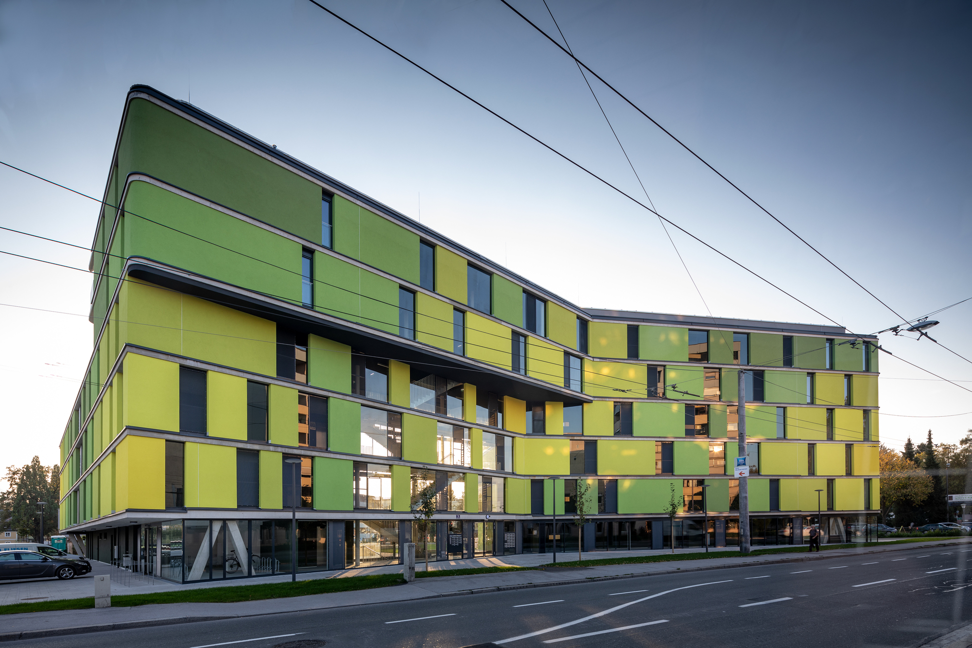 Long facade showing the chequered yellow and green panel composition with ground-level pilotis beneath a cloudy sky