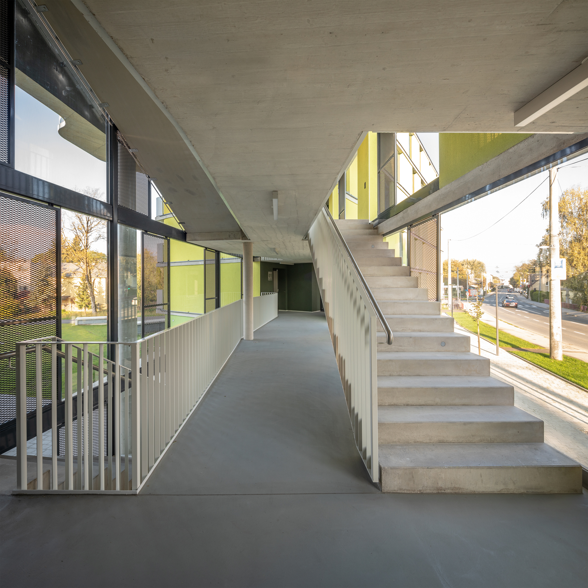 Ground-level circulation corridor with concrete stairs and exposed ceiling slab opening to the yellow facade