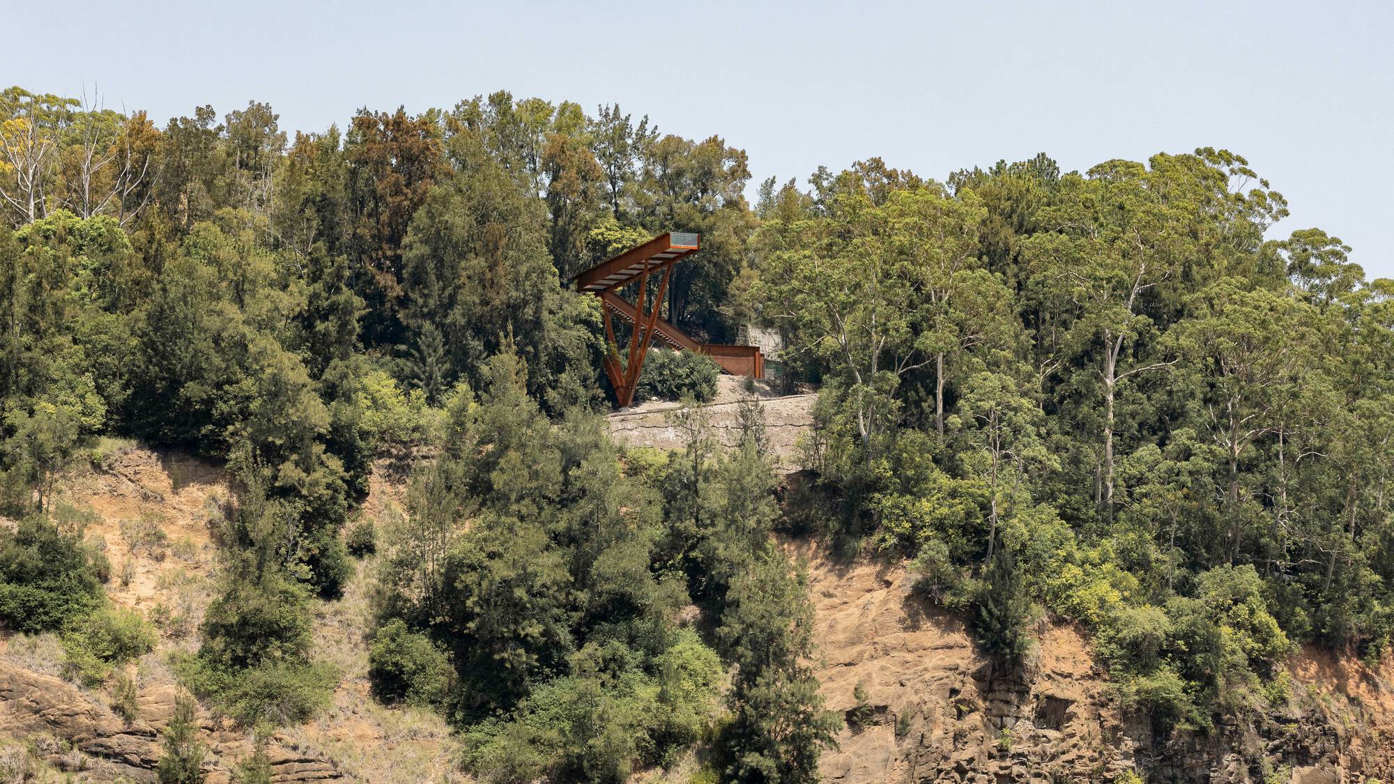 Distant view of the cantilevered steel structure perched atop a vegetated hillside