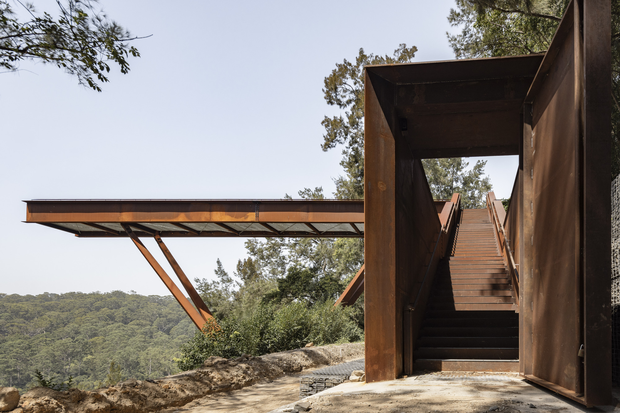 Ground-level view of the cantilevered steel platform and staircase ascending through the steel frame