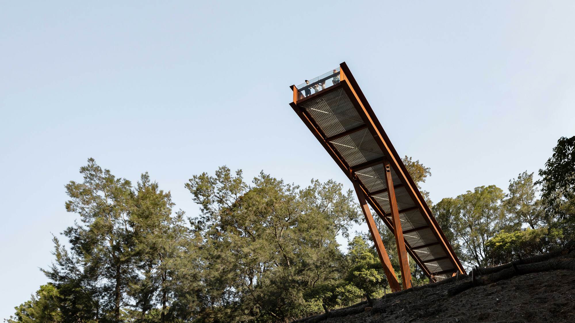 Elevated walkway with weathered steel frame and perforated mesh deck angled against a clear sky