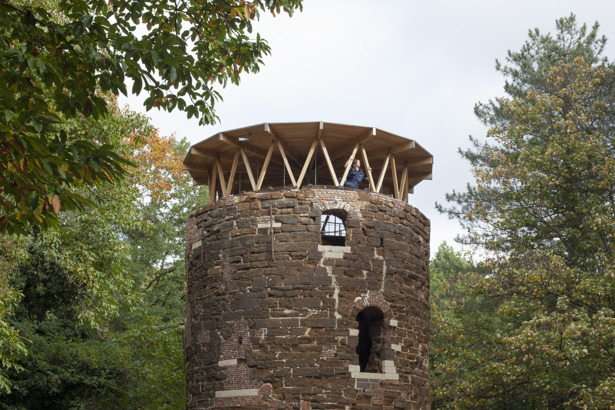 Close view of weathered brick tower with arched openings topped by exposed timber rafters
