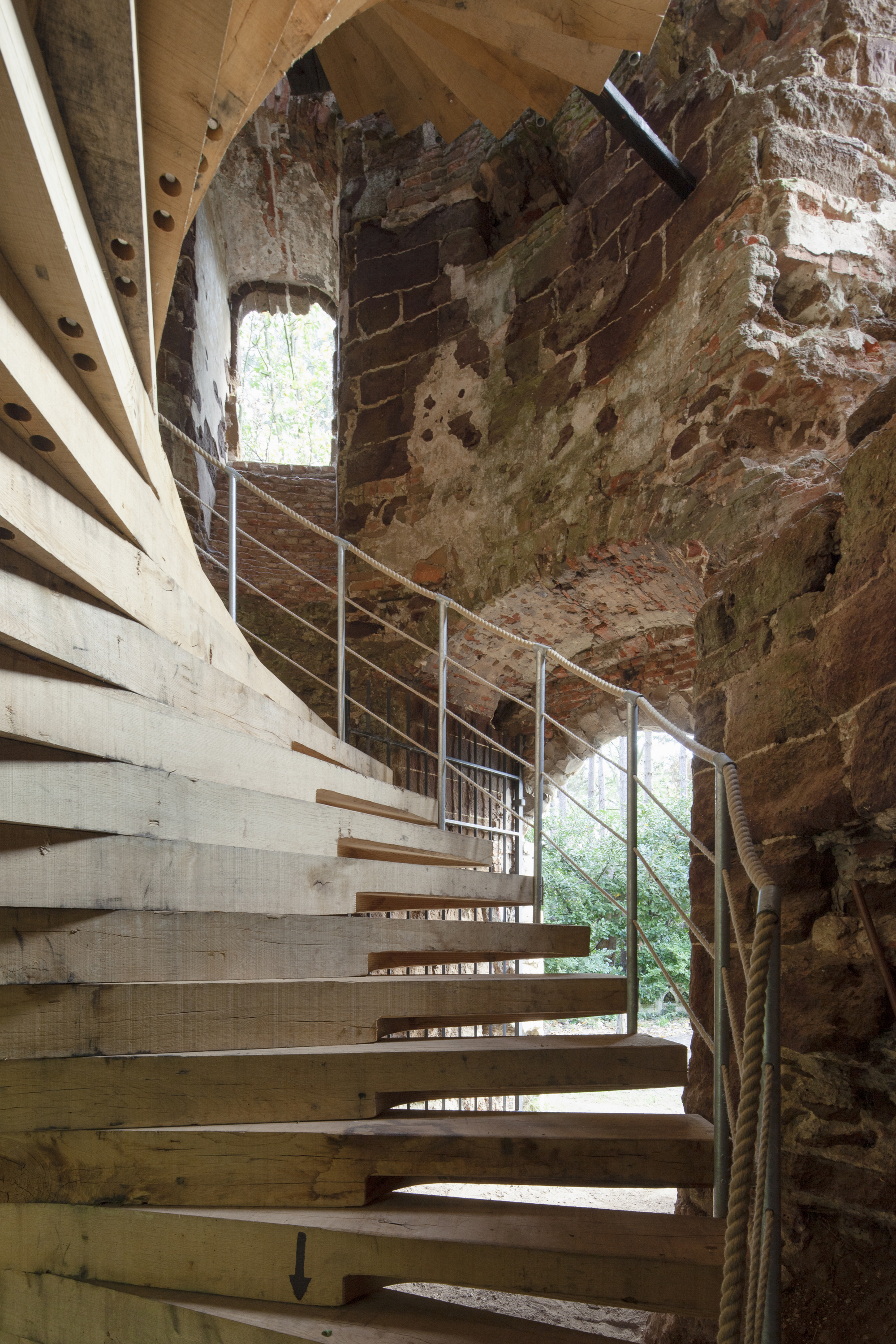 Laminated timber staircase curving along the interior of the deteriorated masonry wall