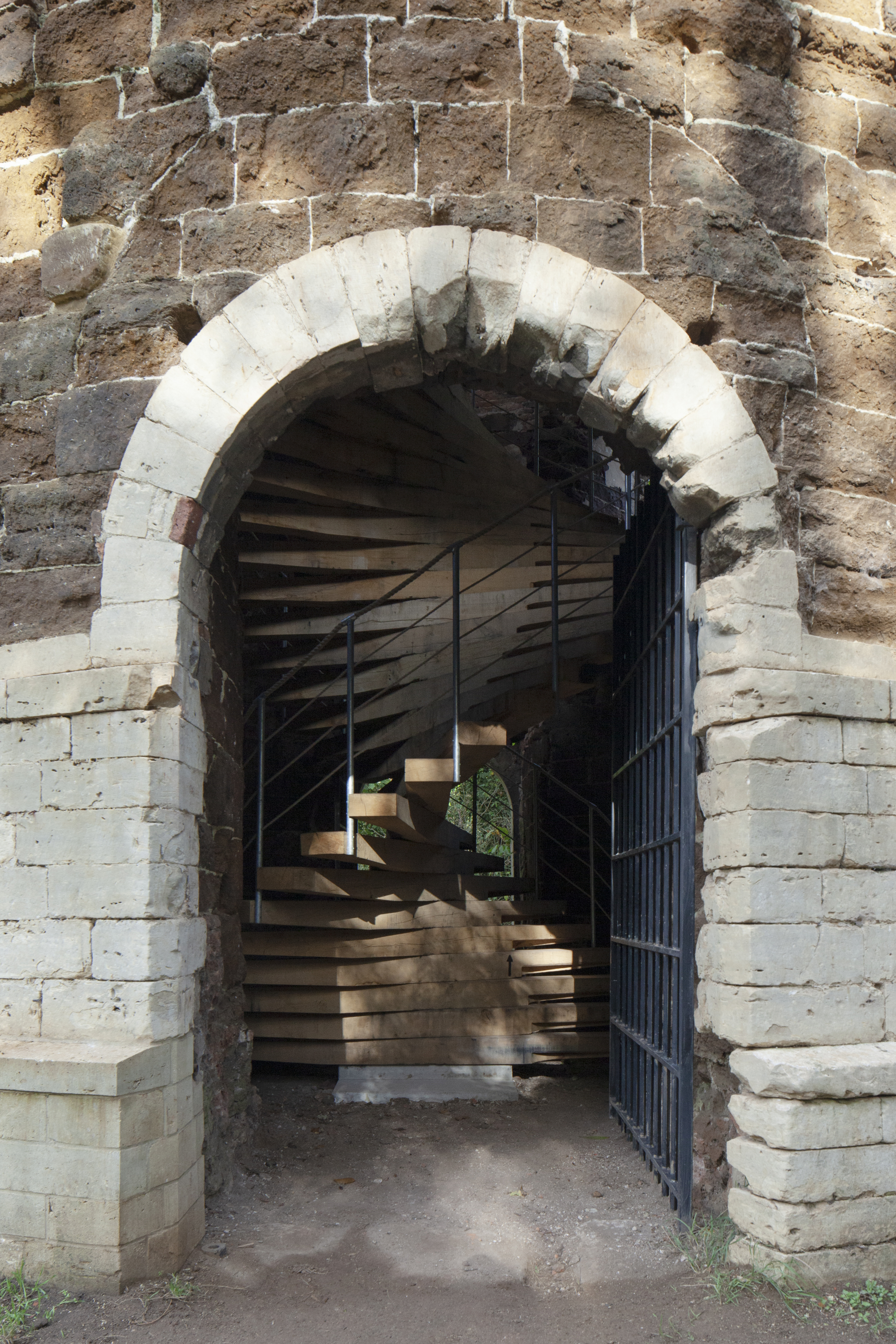 Stone archway with white voussoirs framing a timber staircase and open metal gate beyond