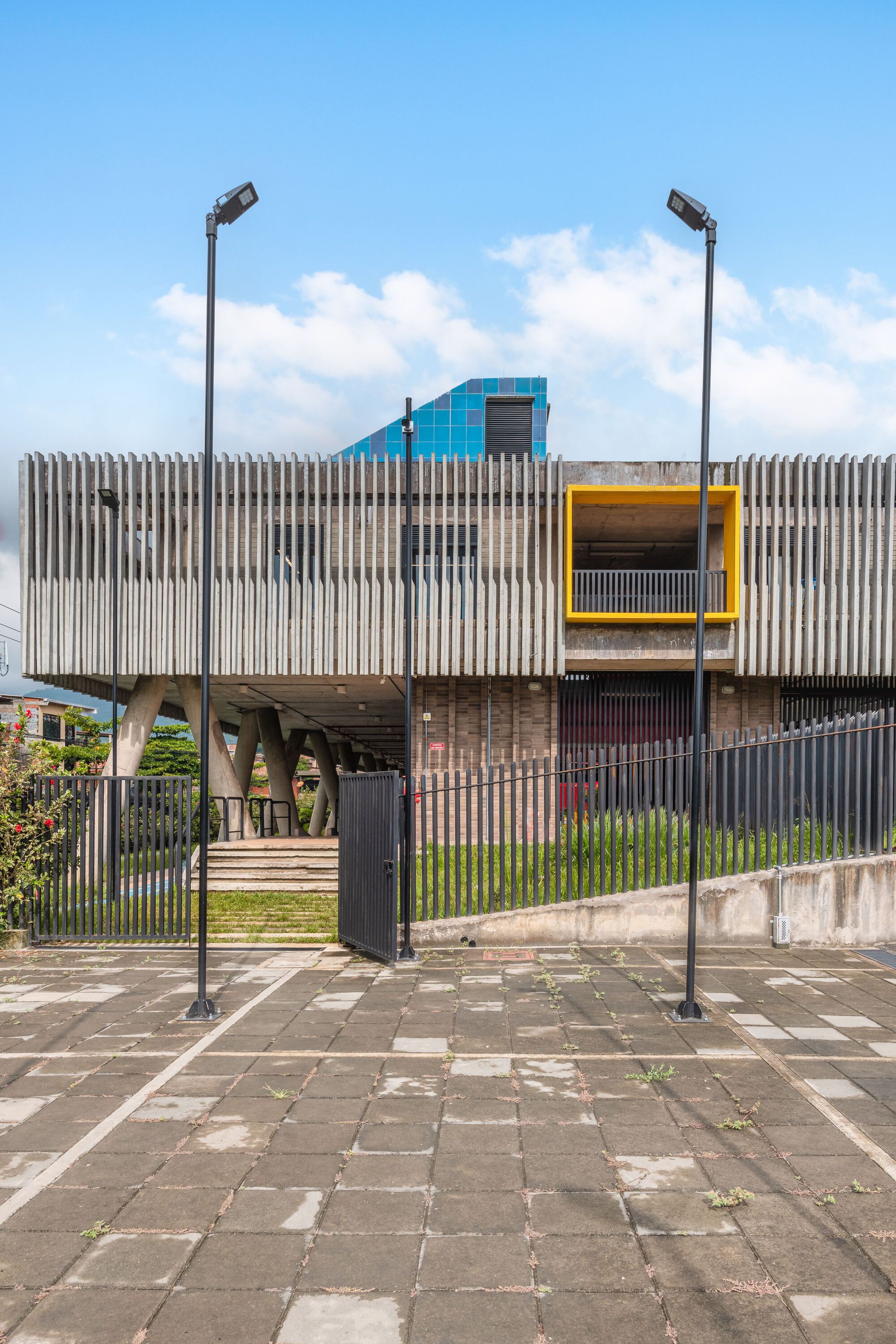 Street view of the vertical corrugated metal facade with yellow-framed openings beneath a cloudy sky