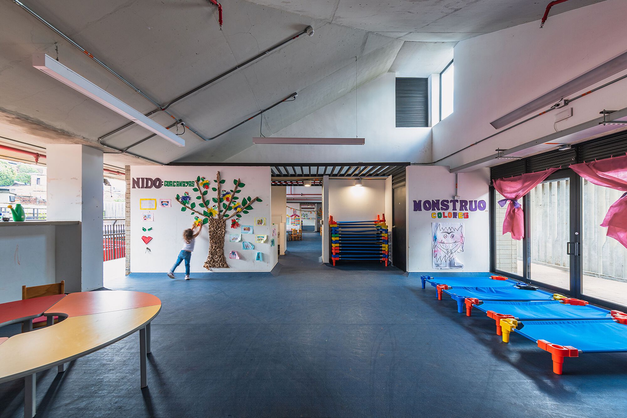 Open interior hall with exposed concrete ceiling, decorative wall murals and a child passing through