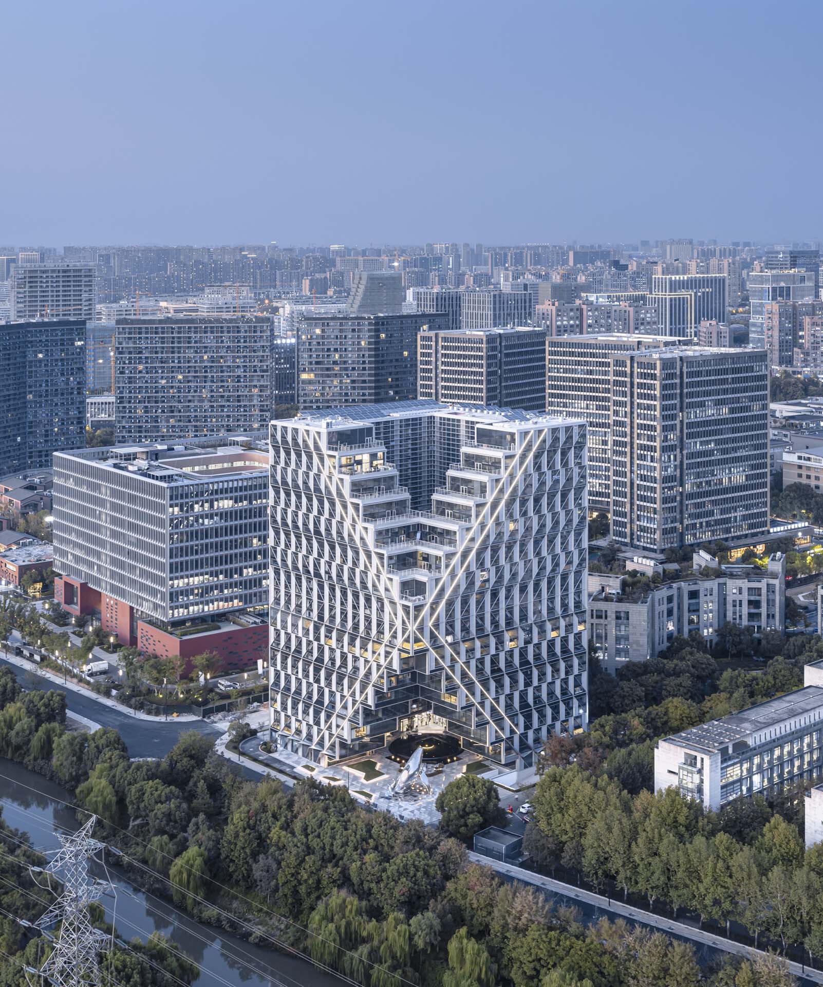 Twin tower forms joined at the base with latticed facades facing a dense urban skyline