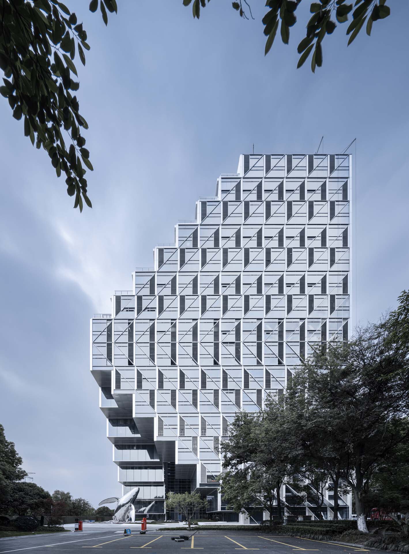 Street view of the ziggurat-shaped tower with its geometric white facade framed by tree branches
