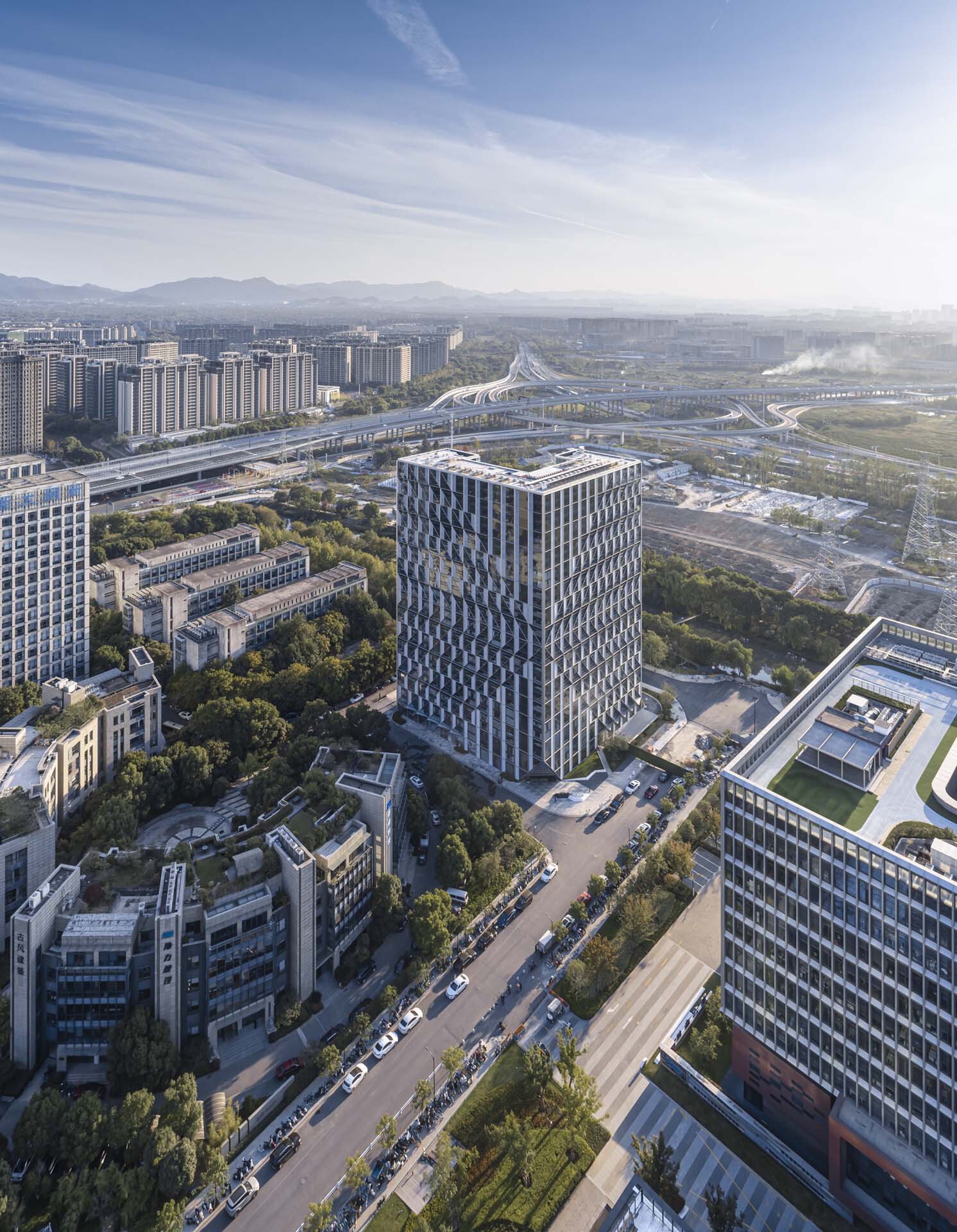 Drone view of the cylindrical tower with diamond-patterned cladding surrounded by highways and green space
