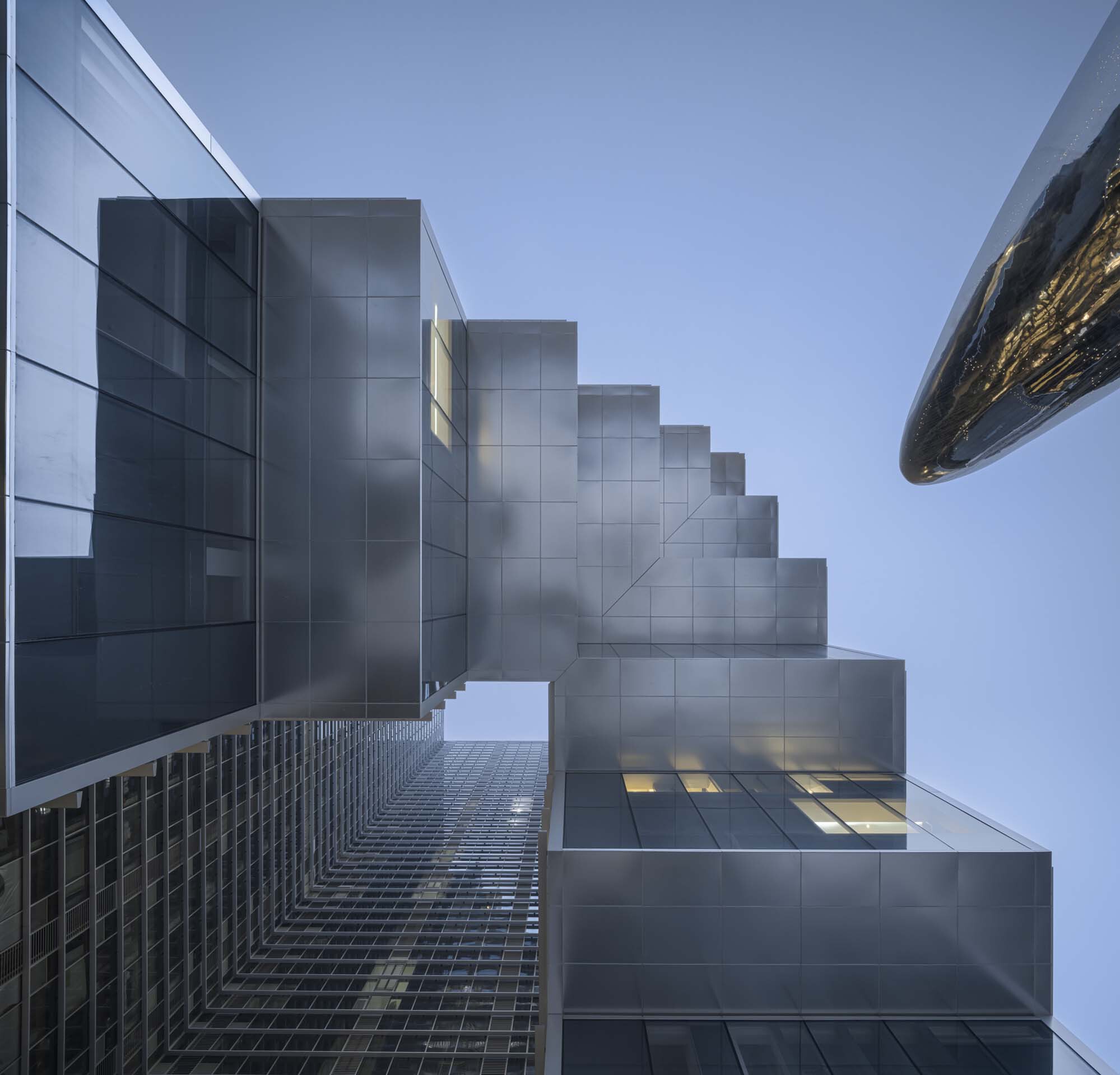 Upward view of the stepped metal panel facade with a glass gridded base at dusk