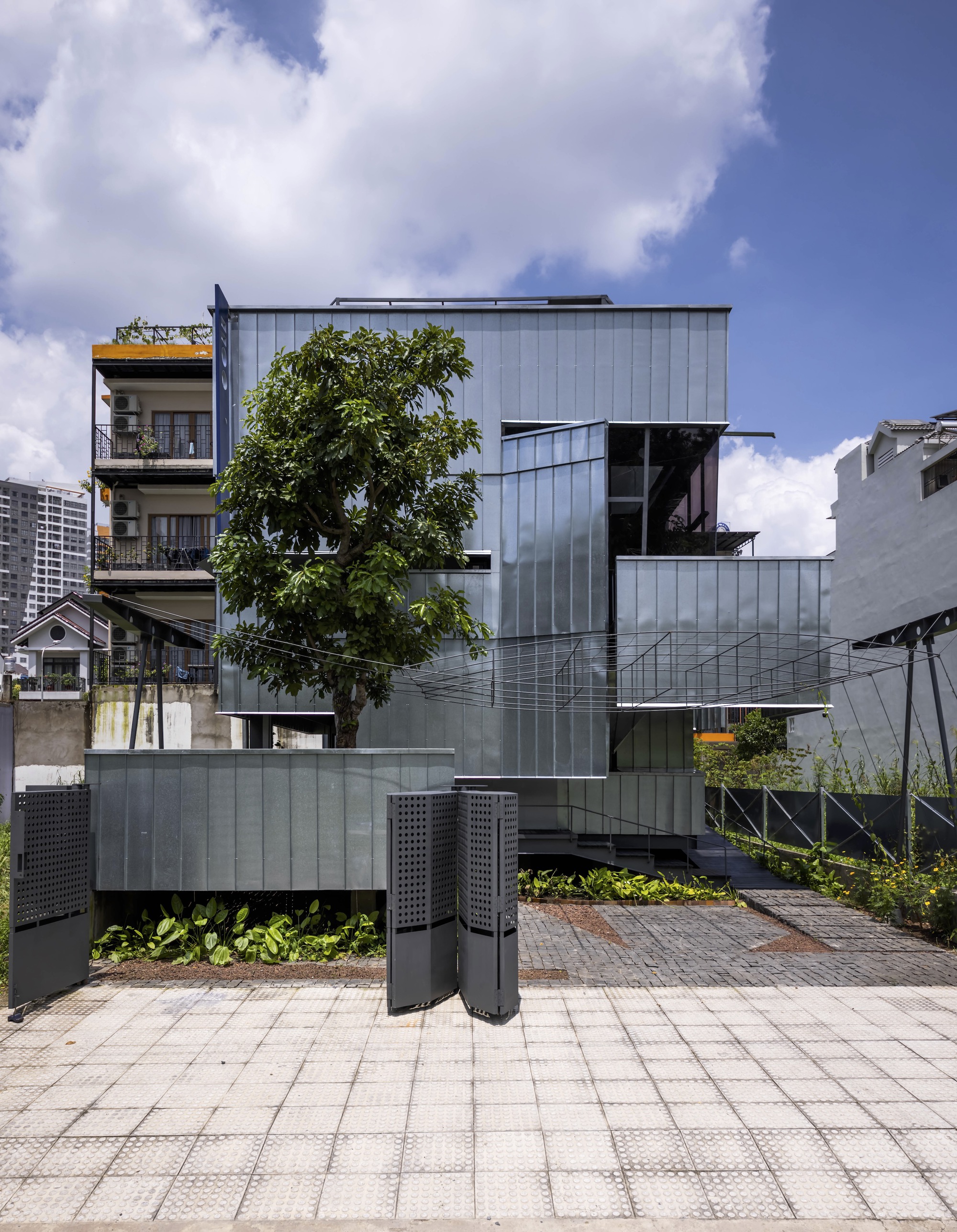 Front elevation showing the stacked metal-clad volumes with a tree emerging through the lower levels