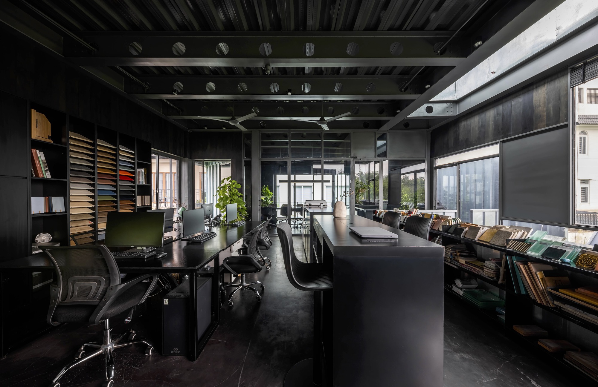 Open-plan office interior with exposed steel trusses, black furnishings and material sample shelving
