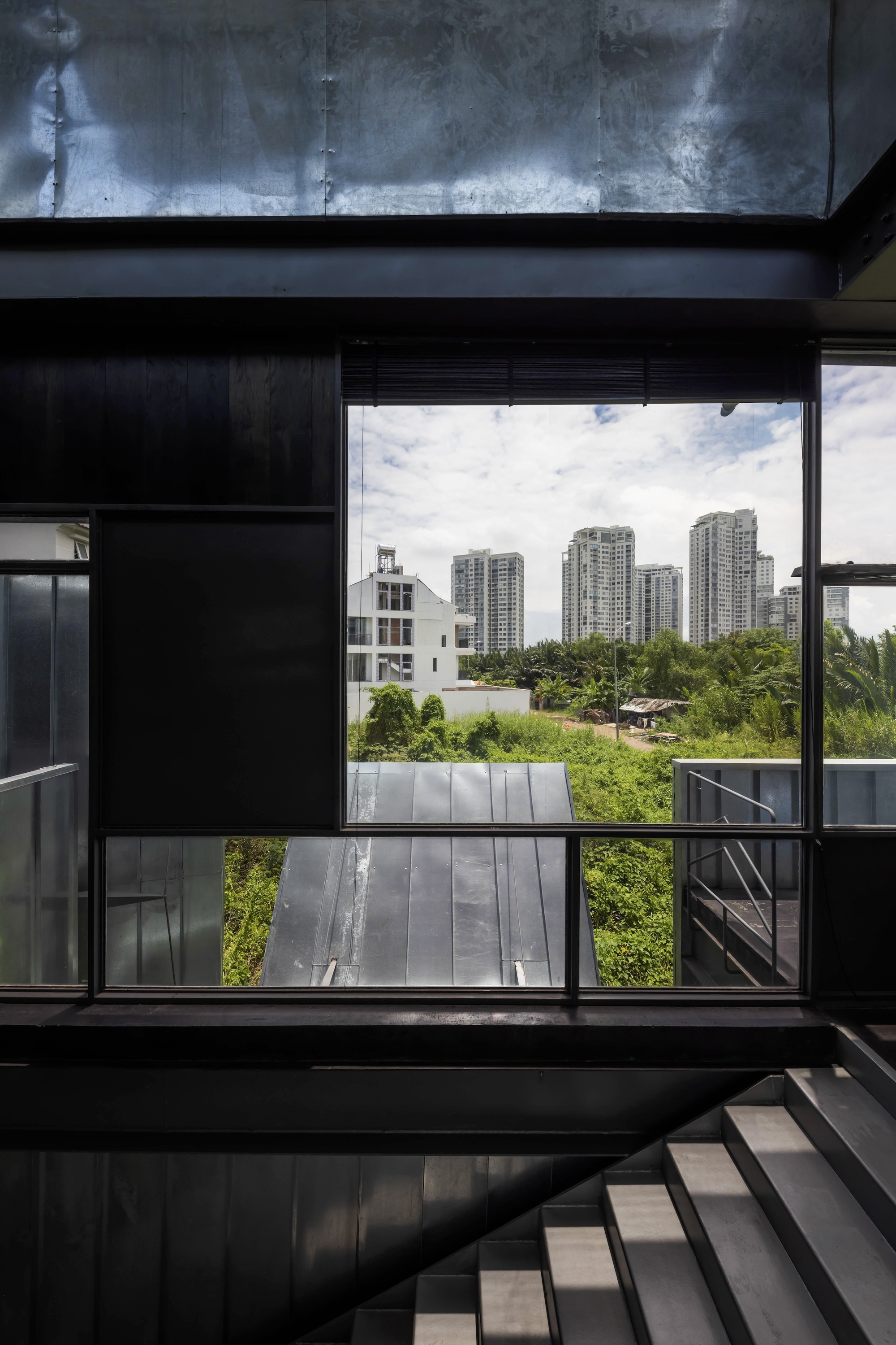 Large window opening framed by blackened steel beams revealing high-rise towers in the distance