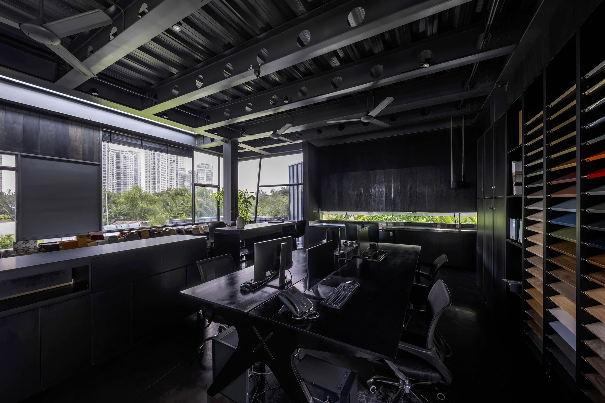Interior office view showing horizontal window slot framing vegetation and distant towers under exposed rafters